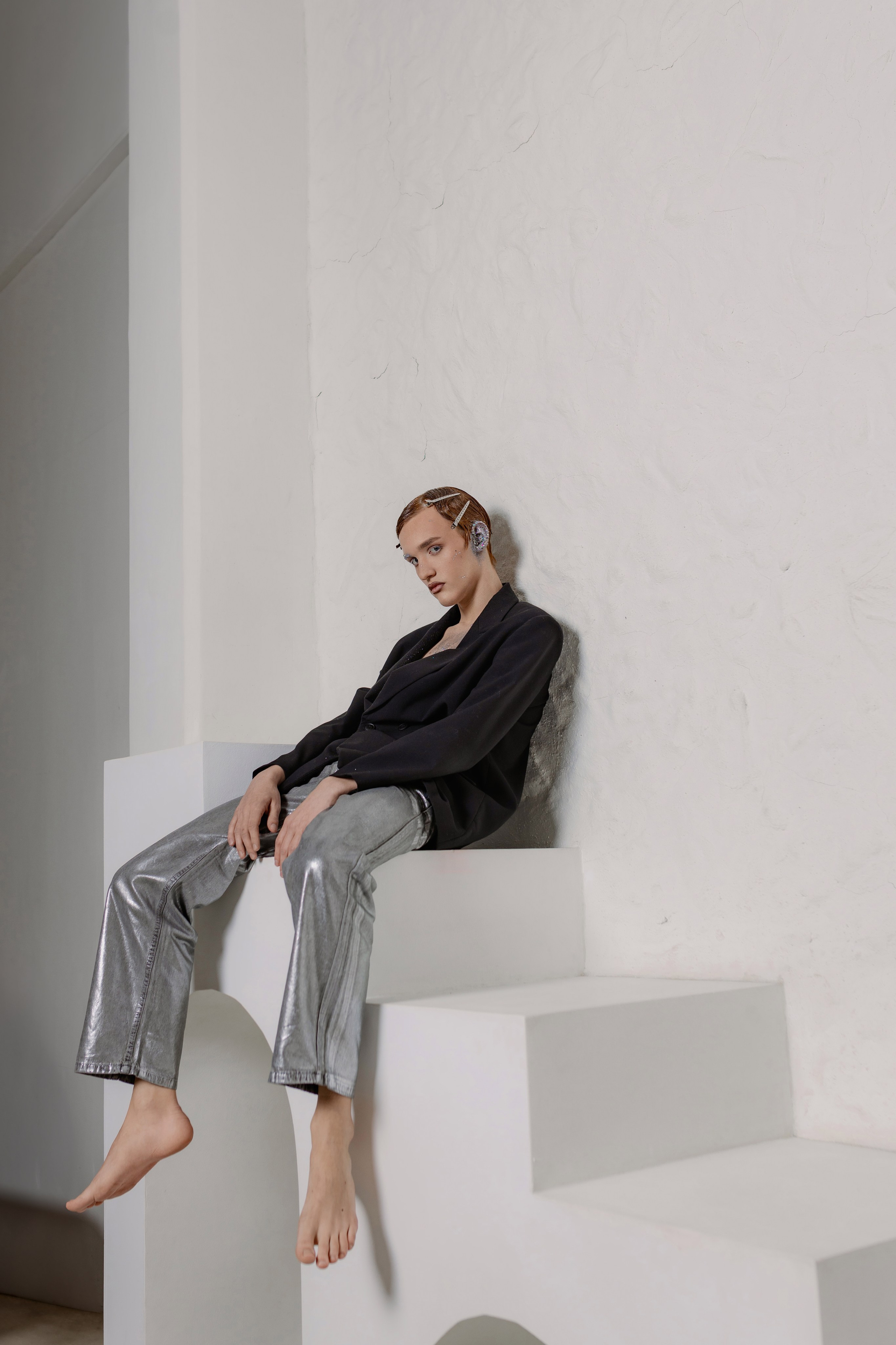 Парень с зализанными волосами в пиджаке на голое тело и брюках металлик. Образ в стиле новой роскоши: сияющая ткань, обнажённая грудь, уверенный взгляд. Fashion-съёмка: мужская модель в наряде металлик на фоне нейтрального фона. 