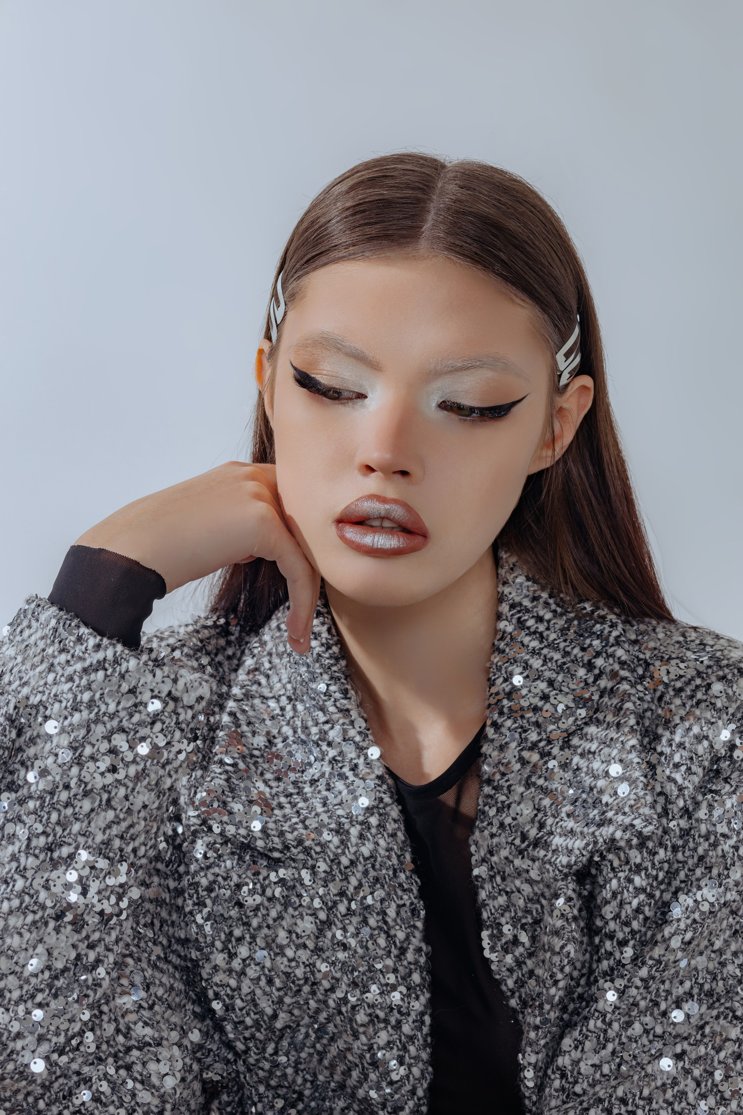 Девушка в блестящем серебряном пальто в пол, макияж в стальном стиле. Портрет с ярким металлическим мейком и длинным пальто с пайетками. Образ в духе будущего: серебро, сияние, дерзкий взгляд