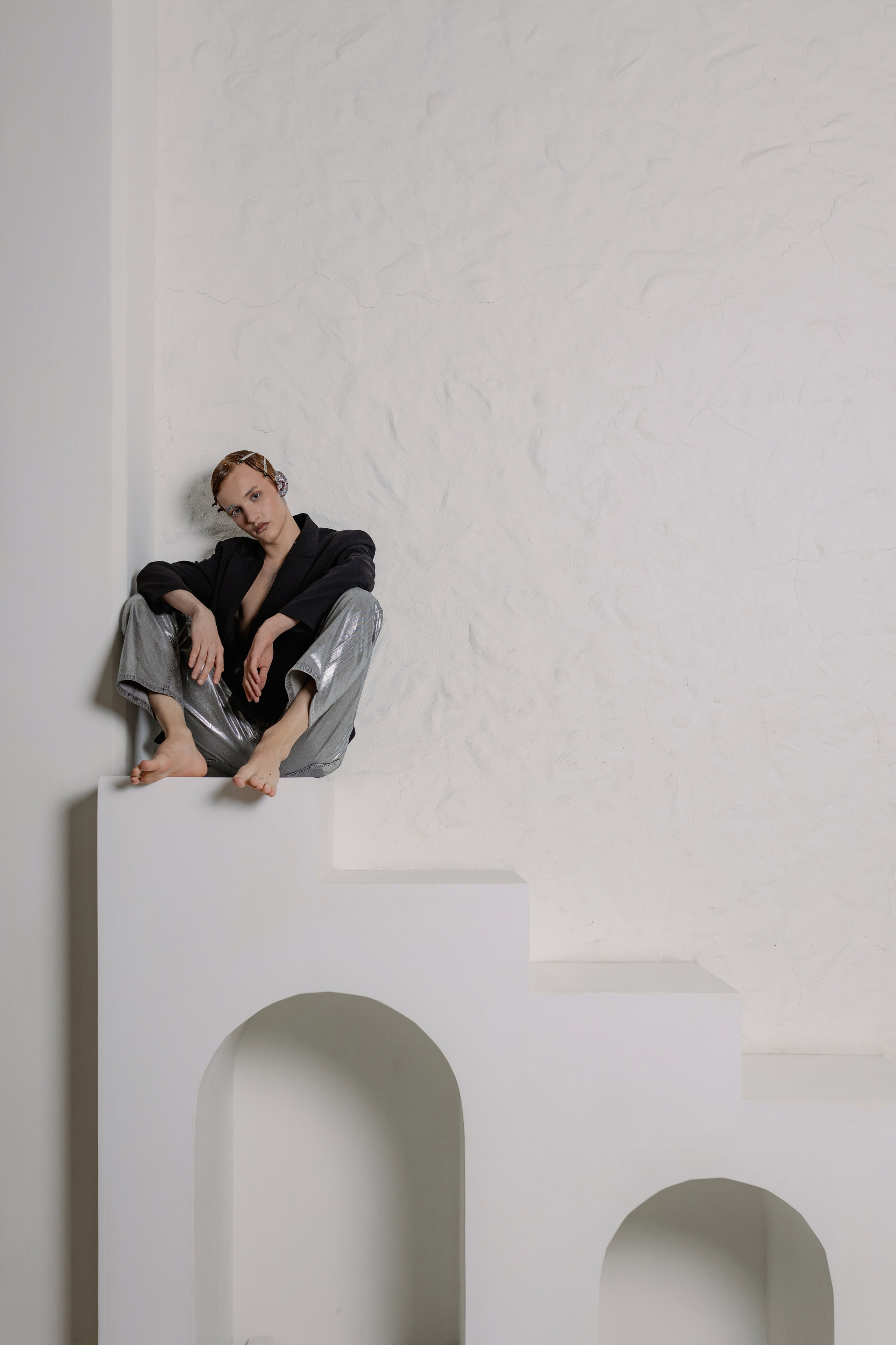 Парень с зализанными волосами в пиджаке на голое тело и брюках металлик. Образ в стиле новой роскоши: сияющая ткань, обнажённая грудь, уверенный взгляд. Fashion-съёмка: мужская модель в наряде металлик на фоне нейтрального фона. 