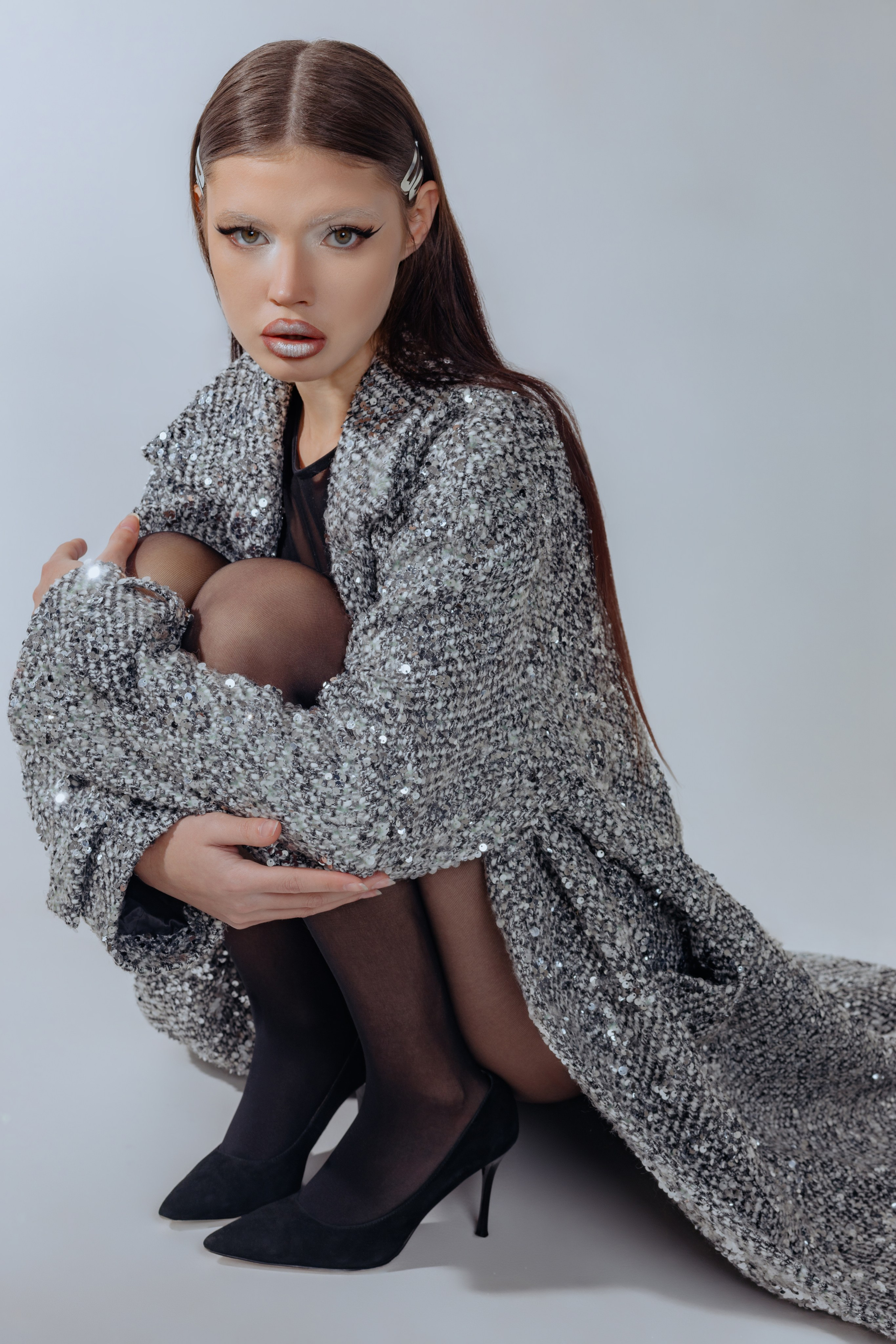 Девушка в блестящем серебряном пальто в пол, макияж в стальном стиле. Портрет с ярким металлическим мейком и длинным пальто с пайетками. Образ в духе будущего: серебро, сияние, дерзкий взгляд