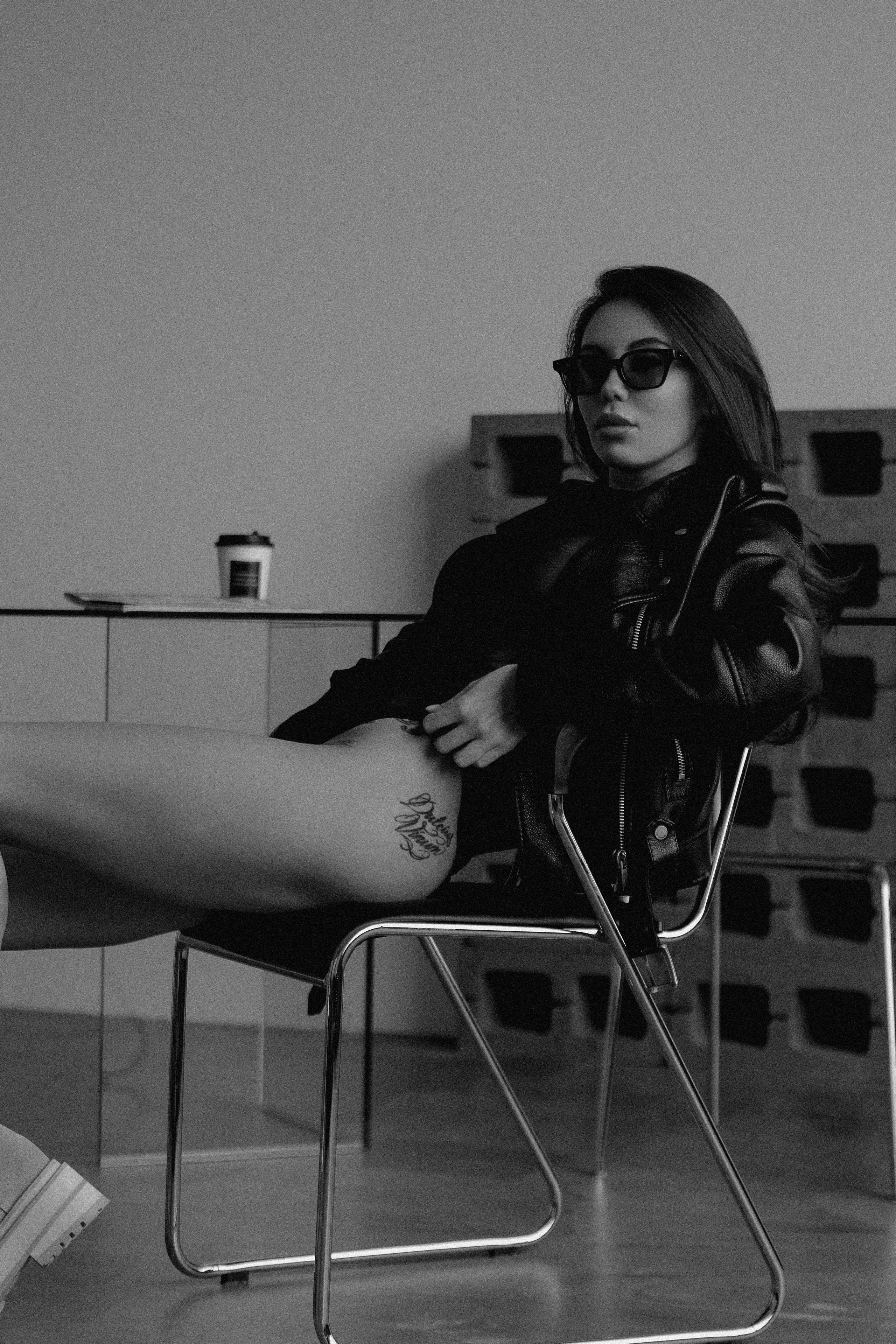 Девушка в боди и в черных очках сидит на стуле