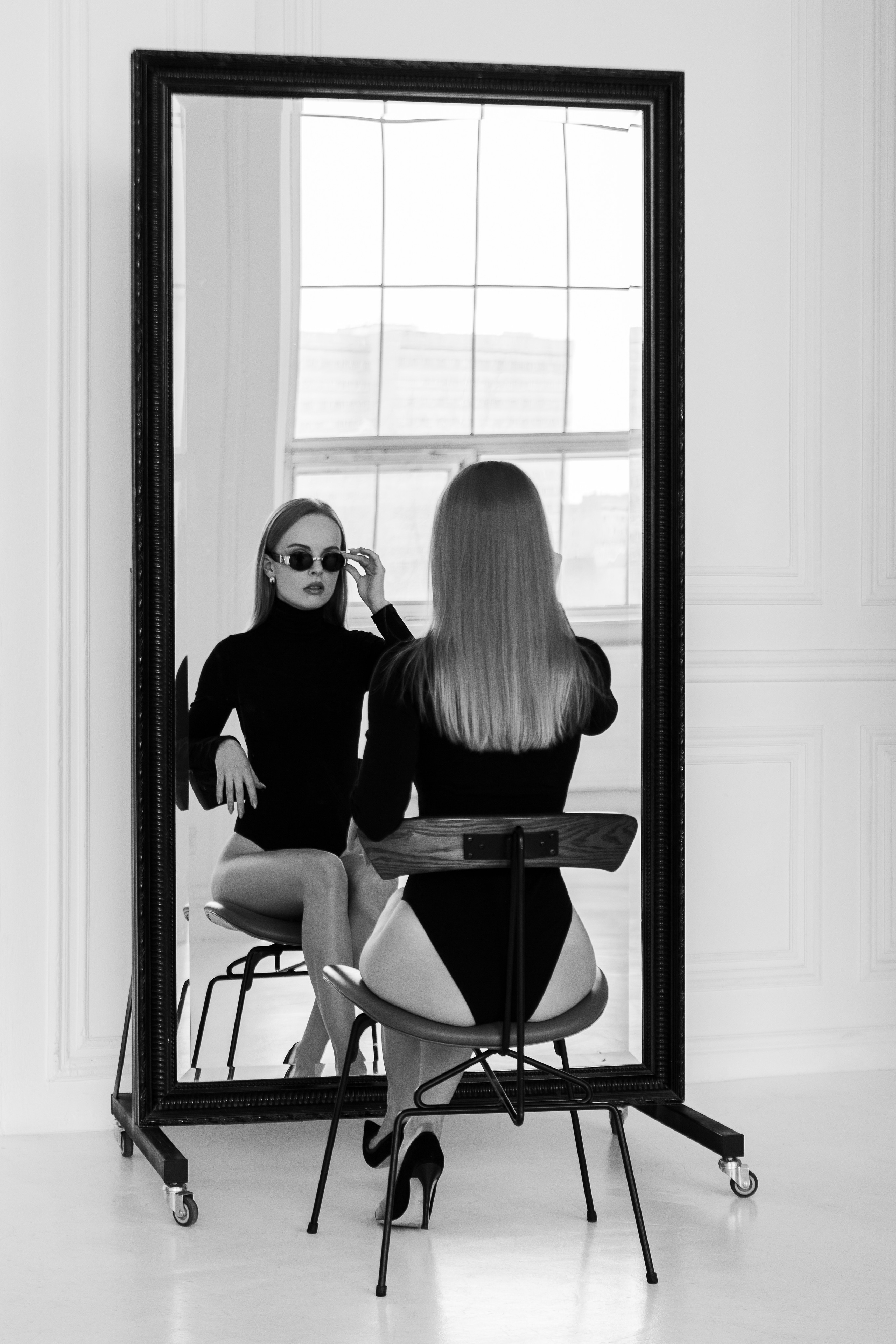 Девушка в боди сидит на стуле напротив зеркала