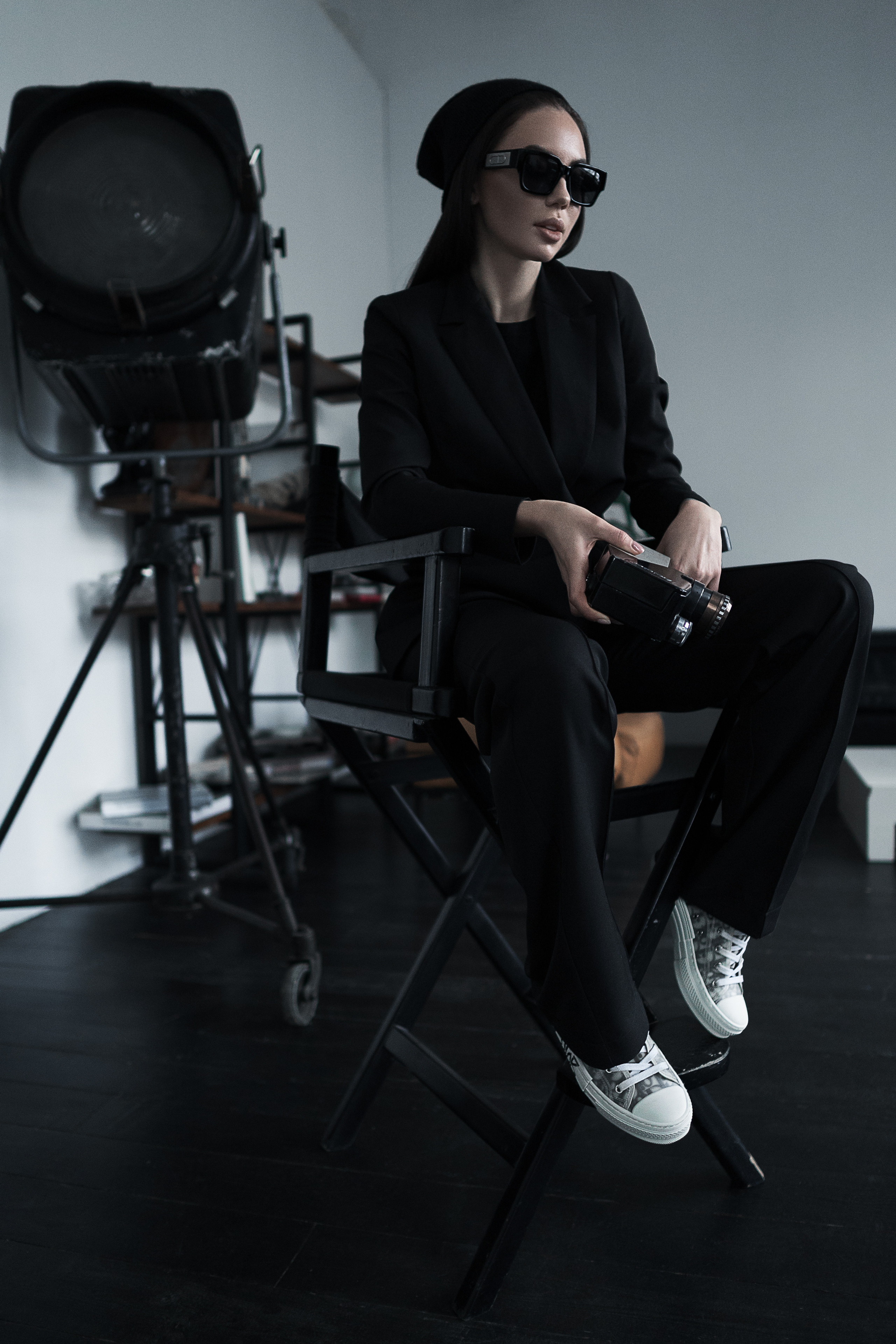 Девушка в очках и строгом костюме сидит в кресле с камерой в руках