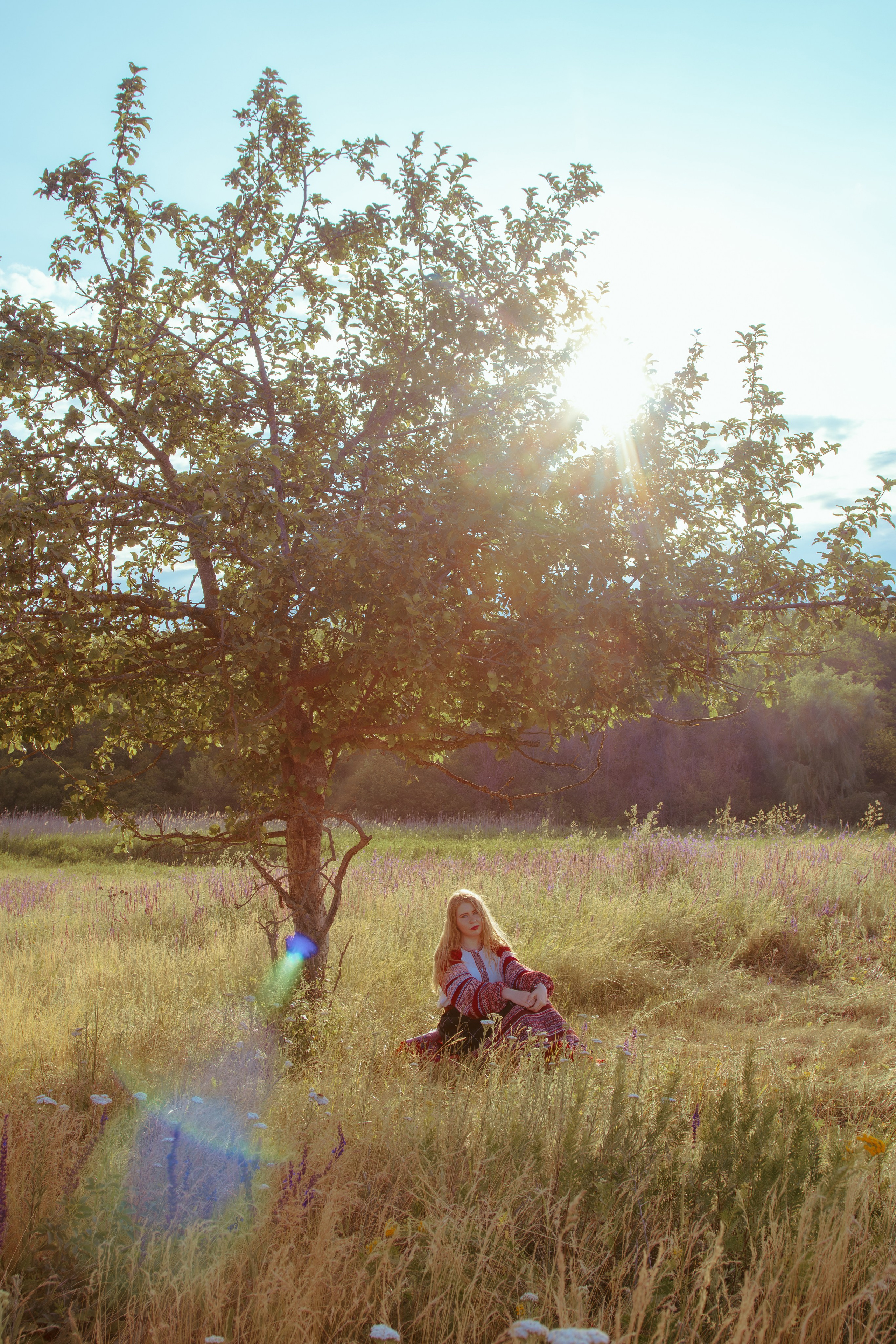 Пейзаж леса и солнца посреди которого находится девушка в красном славянском платье 