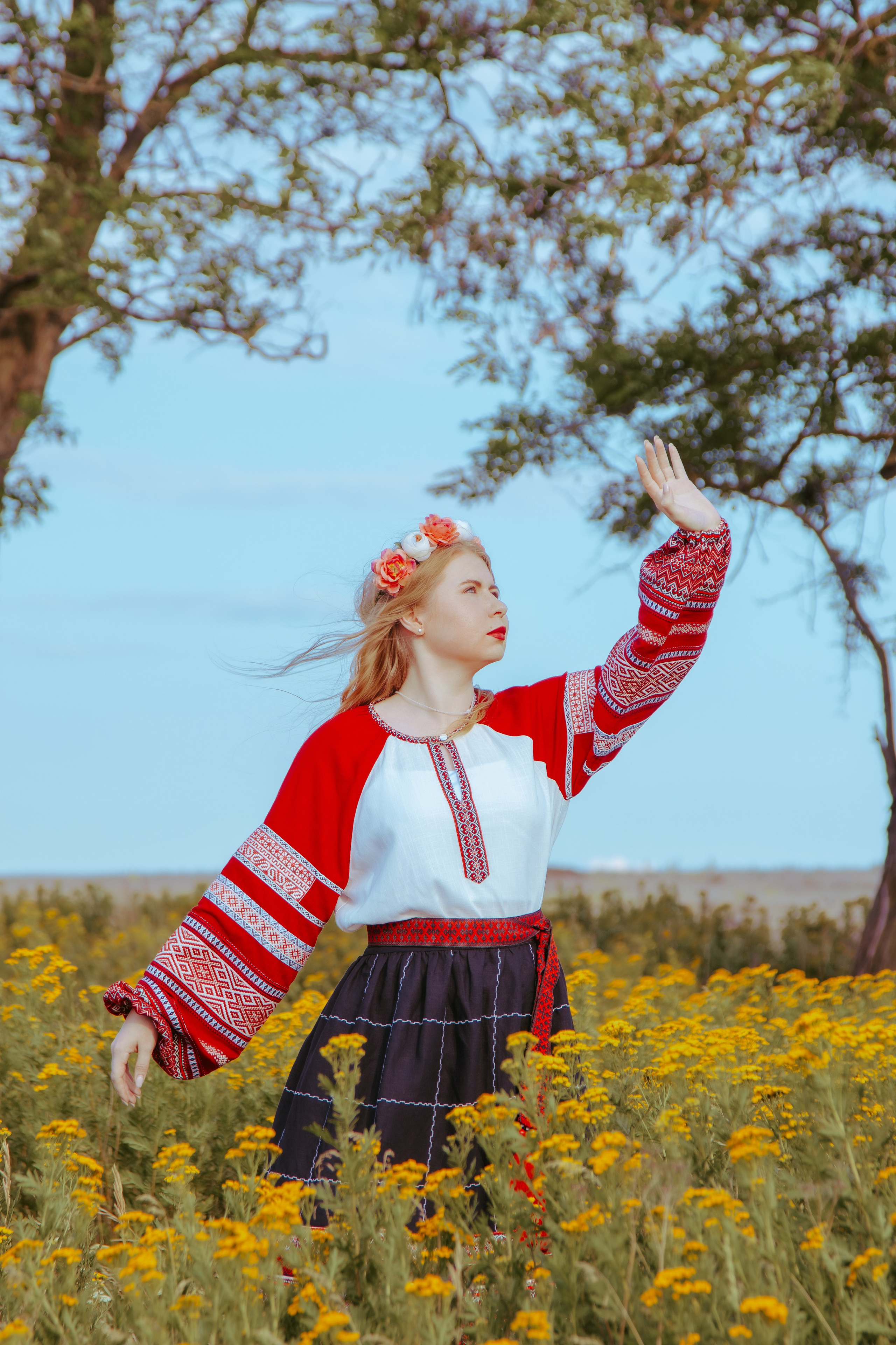 Девушка в славянском платье тянется к небу на фоне голубого неба и жёлтых цветов