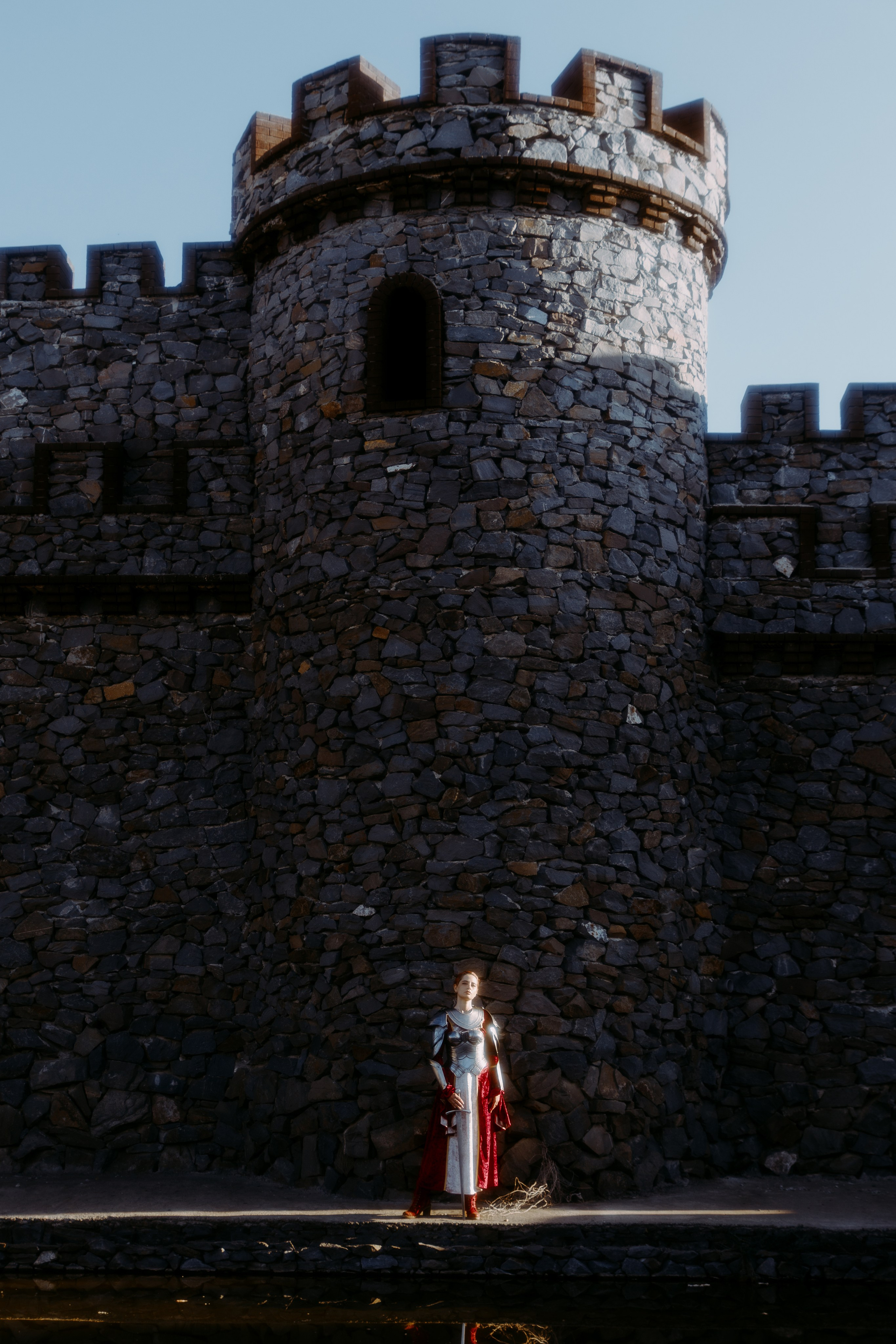 Девушка рыцарь на фоне замка стоит возле воды в полный рост