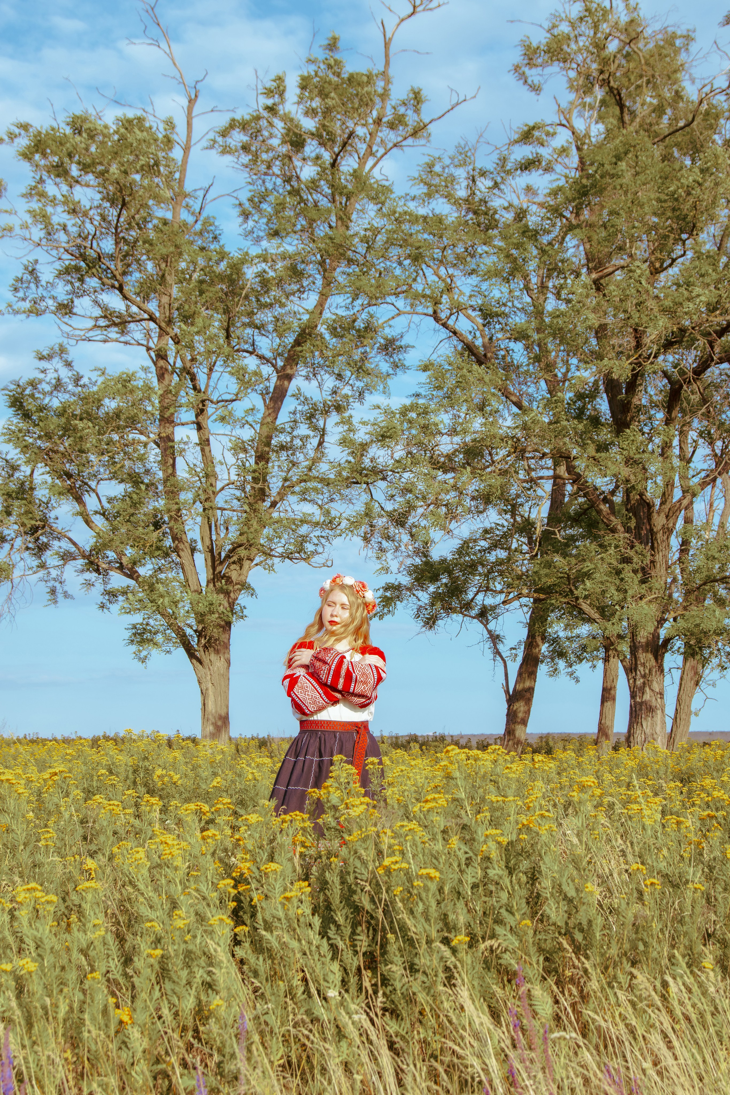 На фоне деревьев стоит девушка в русско-народной одежде 