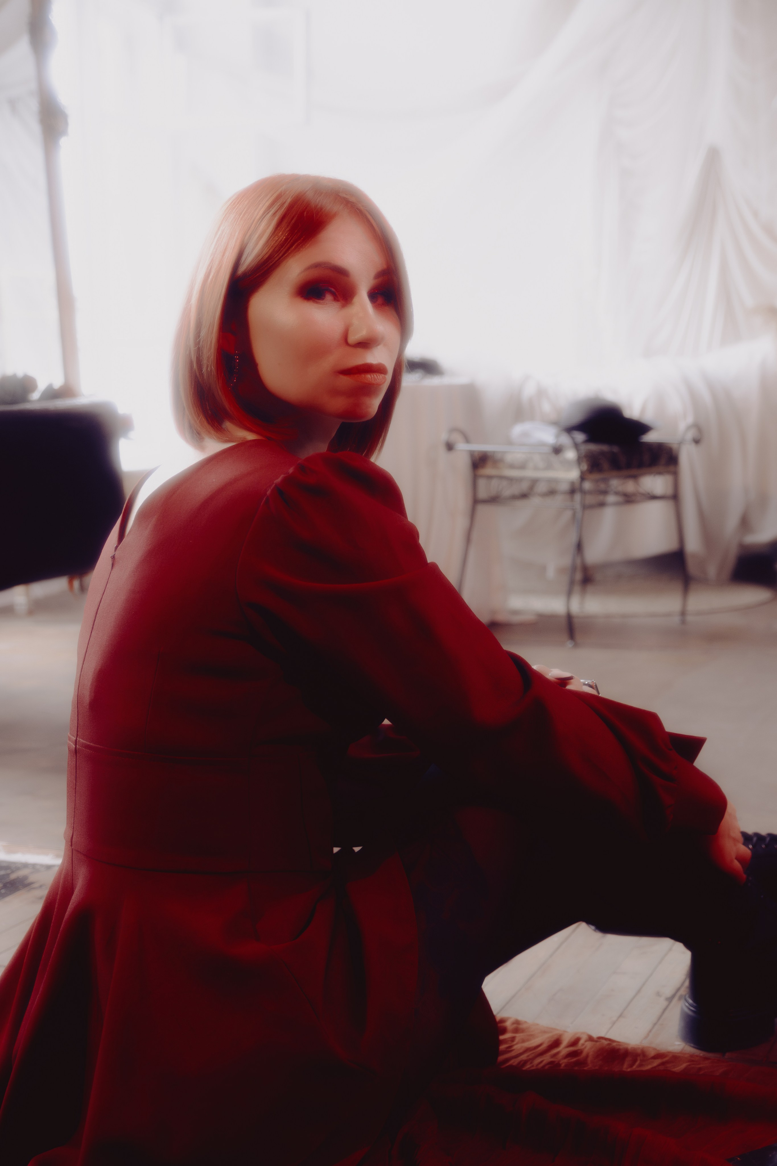 Таролог в расслабленной позе, руки сложены на коленях. Тёплый свет создаёт ощущение уюта и доверия.