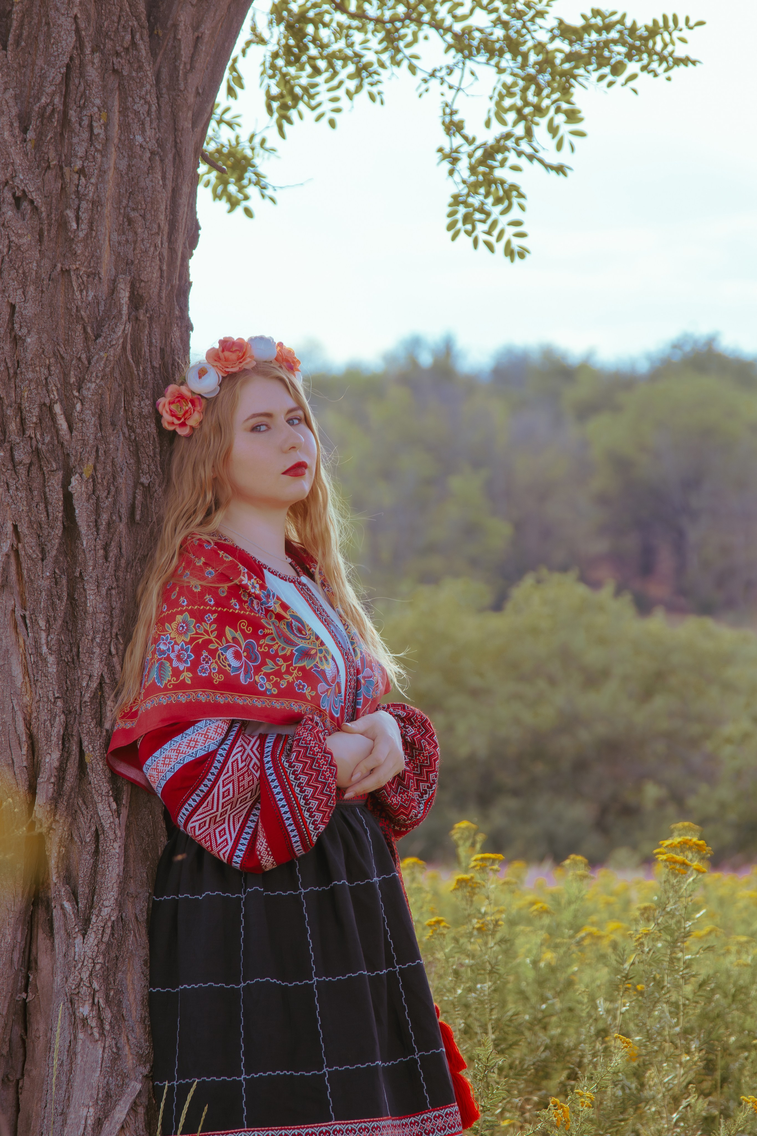 Девушка в славянской одежде стоит на фоне дерева в лесу