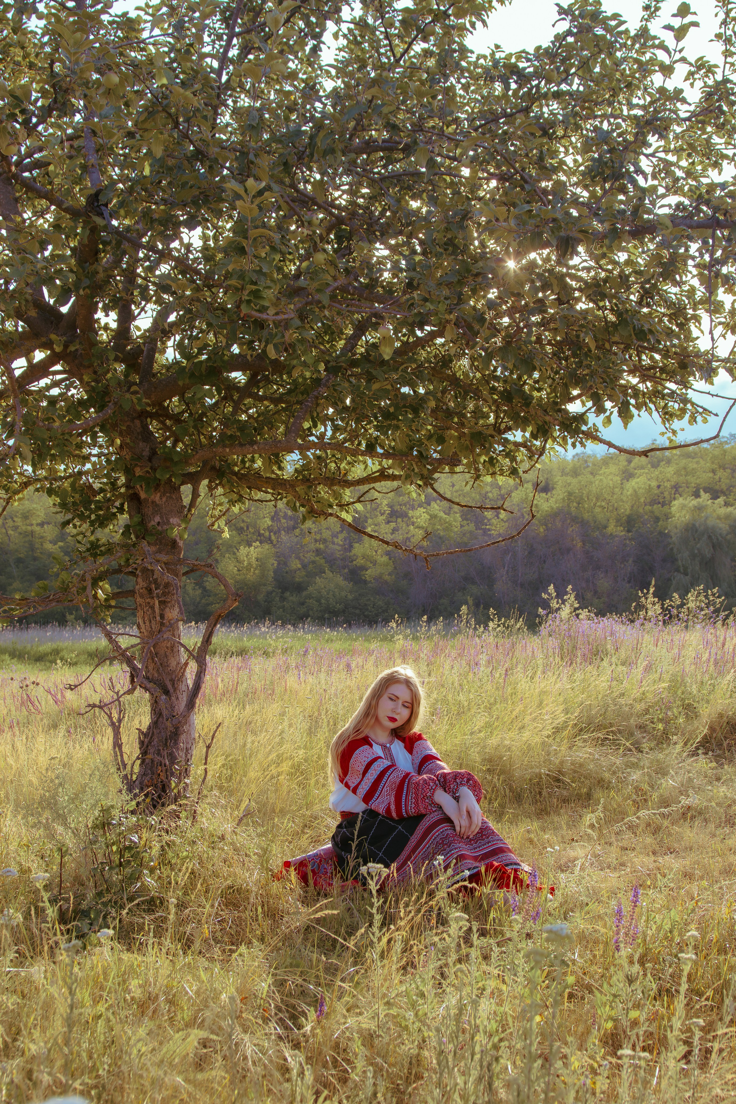 Девушка сидит под деревом в славянской одежде
