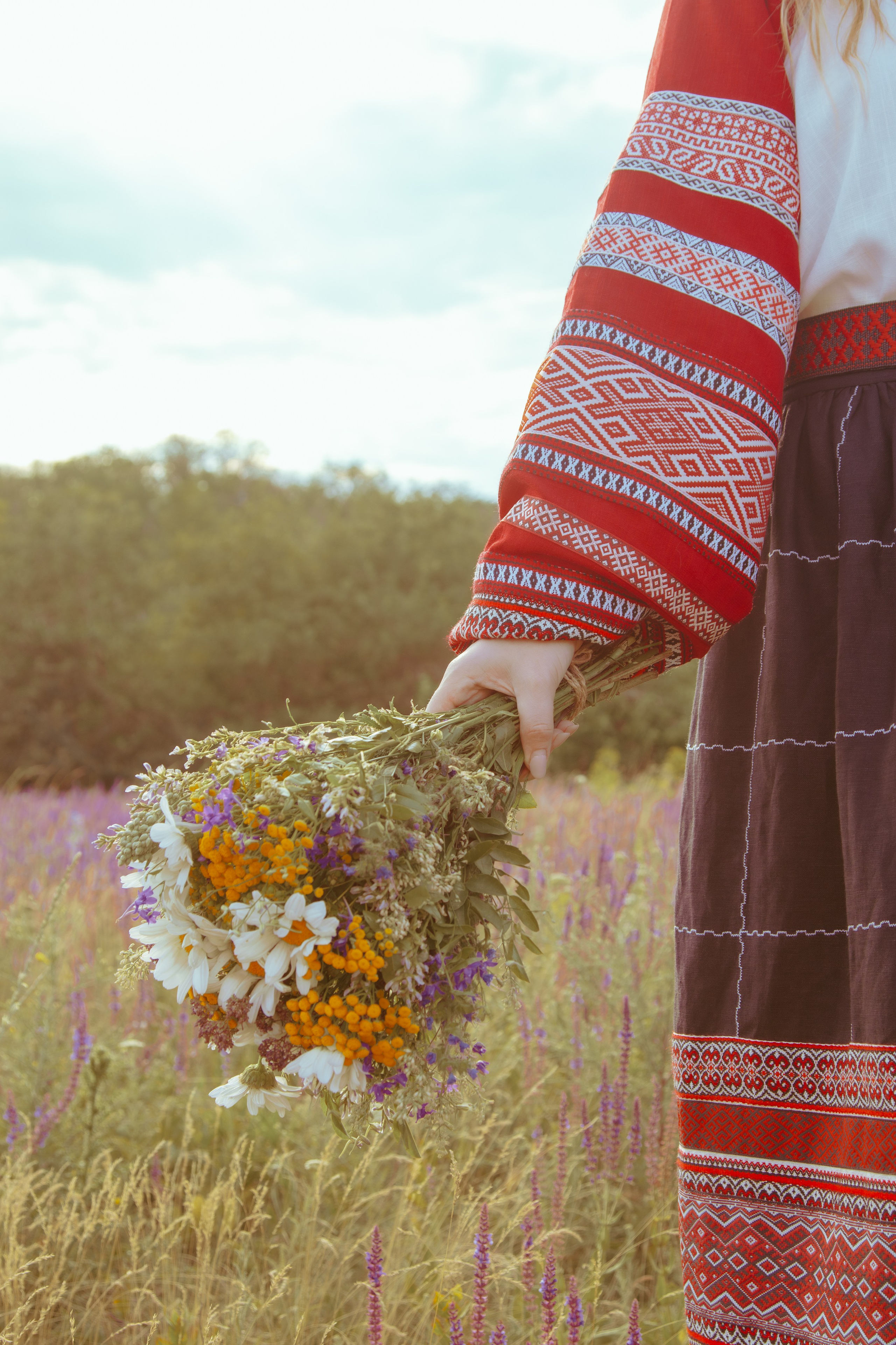 Цветы в руке у славянской девушки на фоне красивого неба и чистого поля