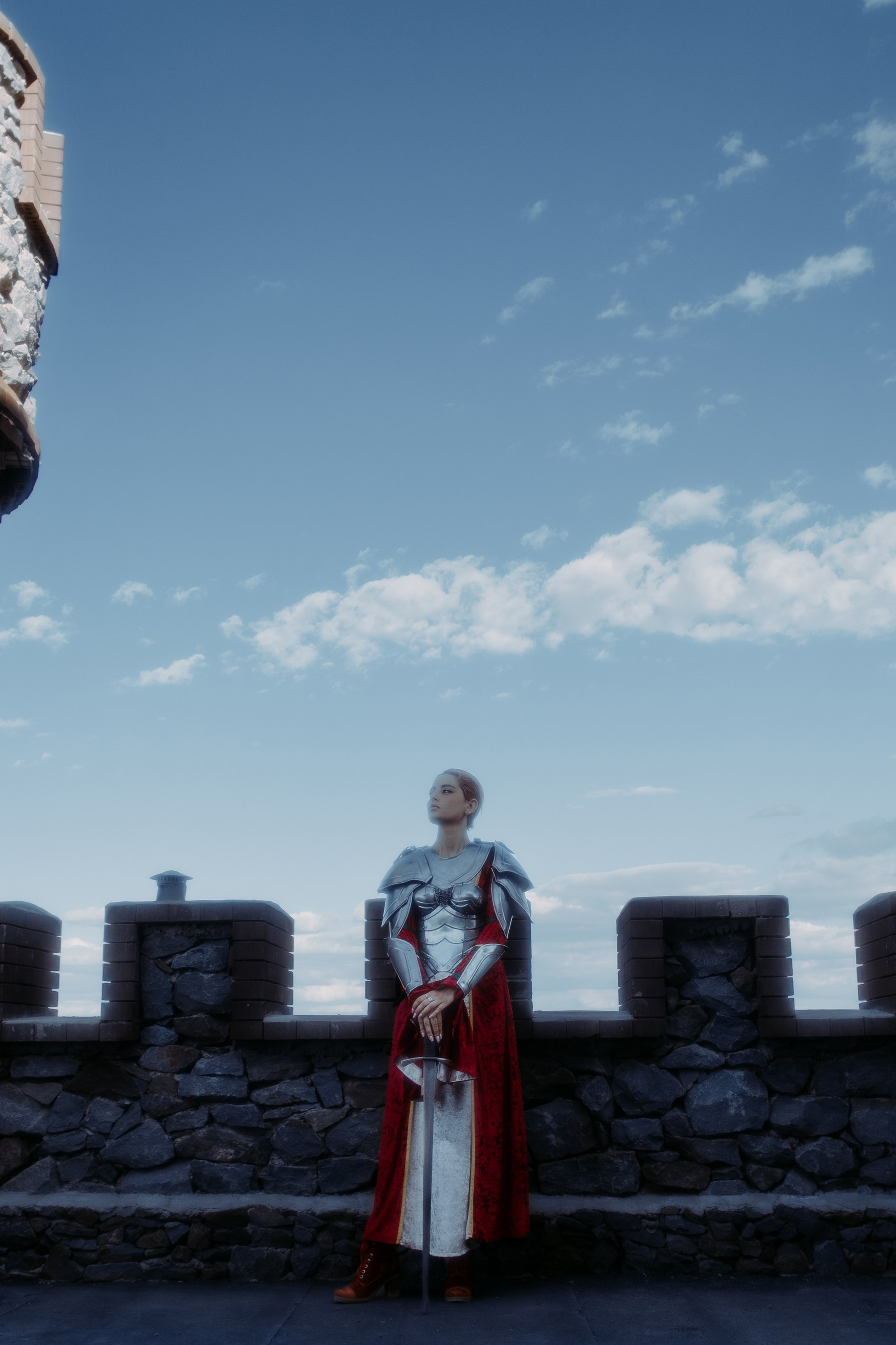 Художественная фотография рыцарского замка, где по середине стоит прекрасная девушка в рыцарском костюме с мечом в руках