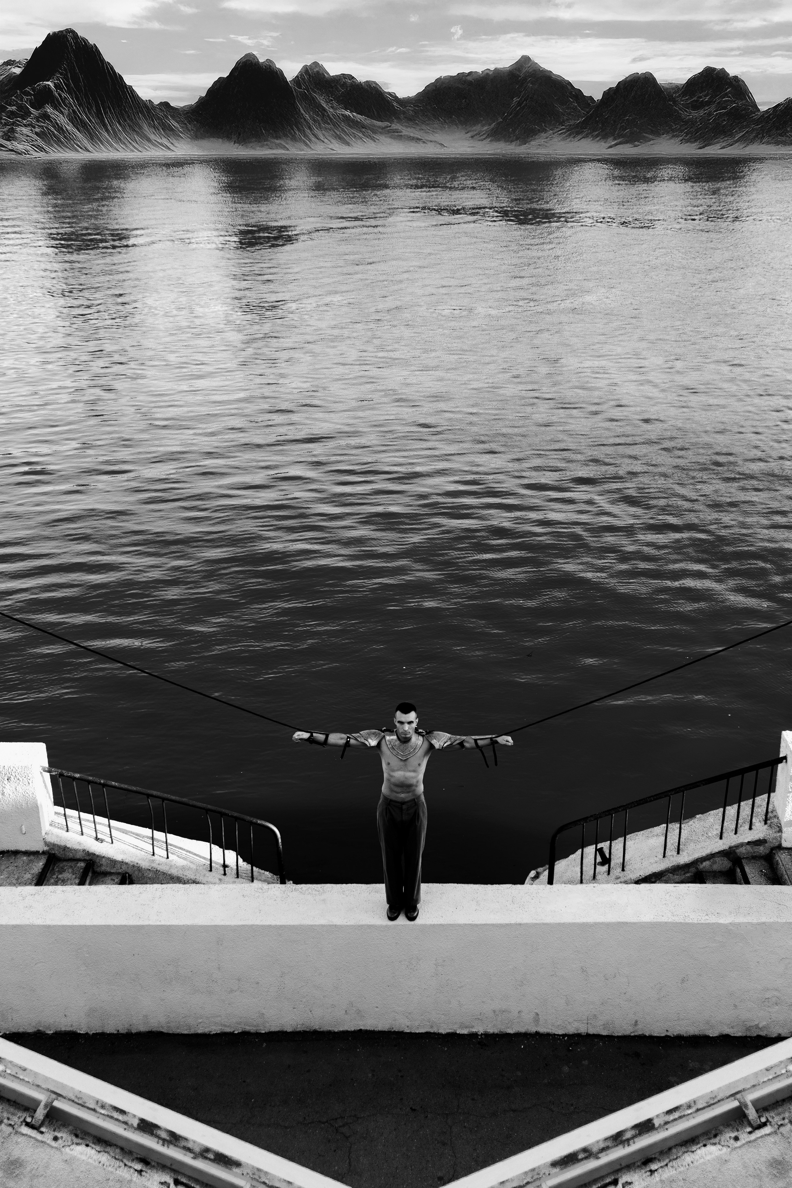 Арт фотография в чёрно белом стиле. На фоне гор и воды мужчина в рыцарских доспехах связан веревкой за руки и растянут в сторону
