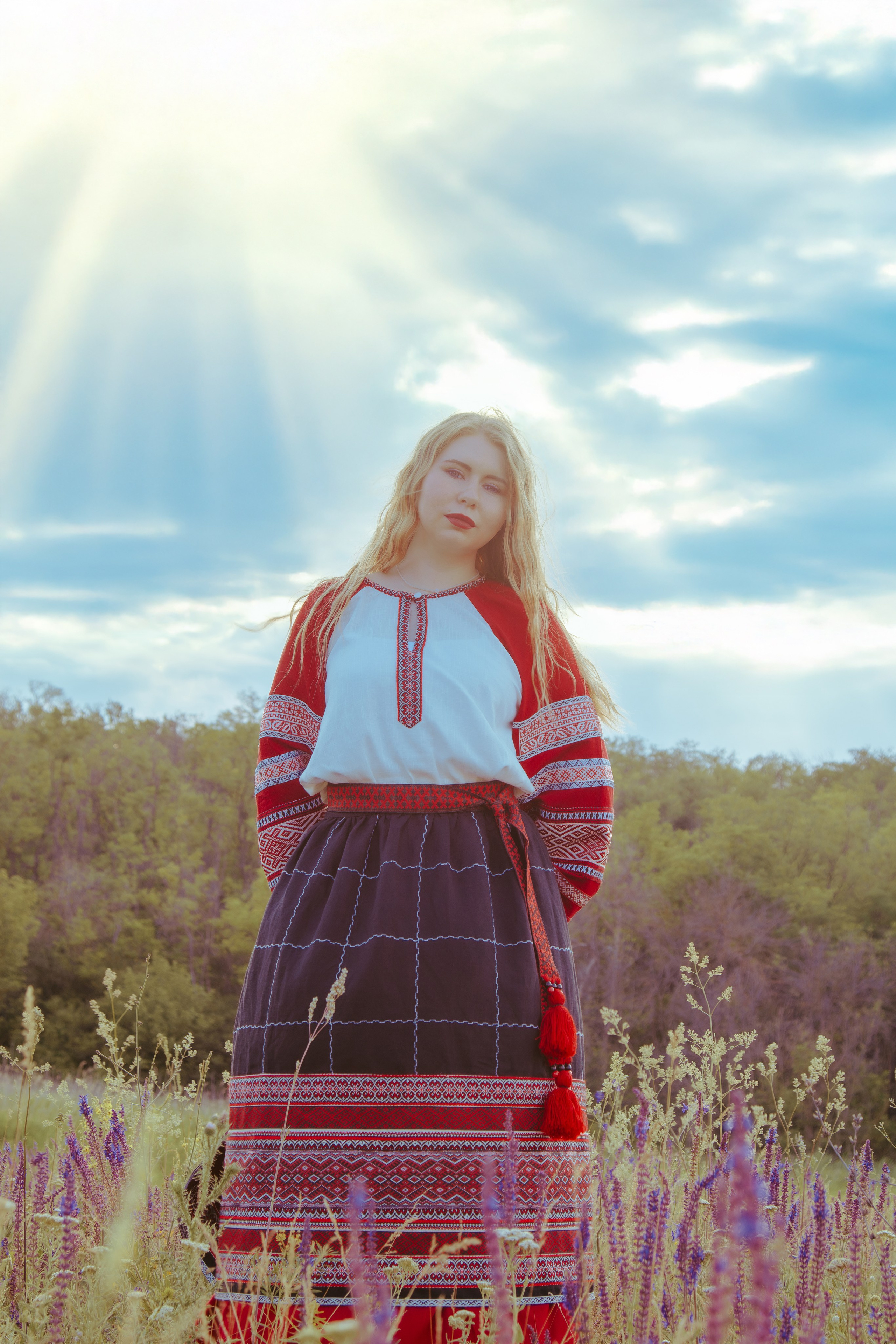 Портрет девушки в славянской одежде с лучами солнца на фоне голубого неба с облаками