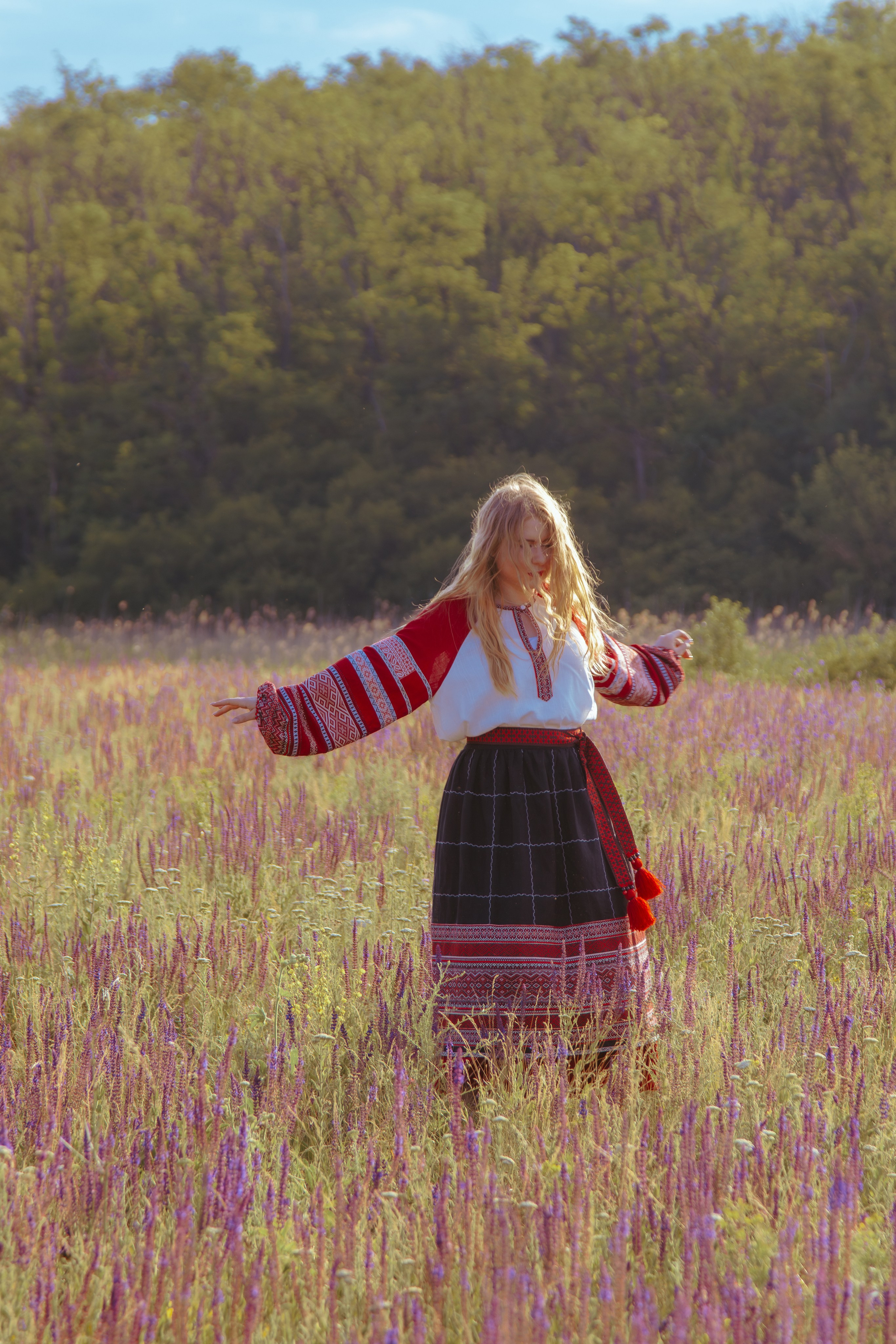Девушка в народном костюме танцует в поле на фоне леса