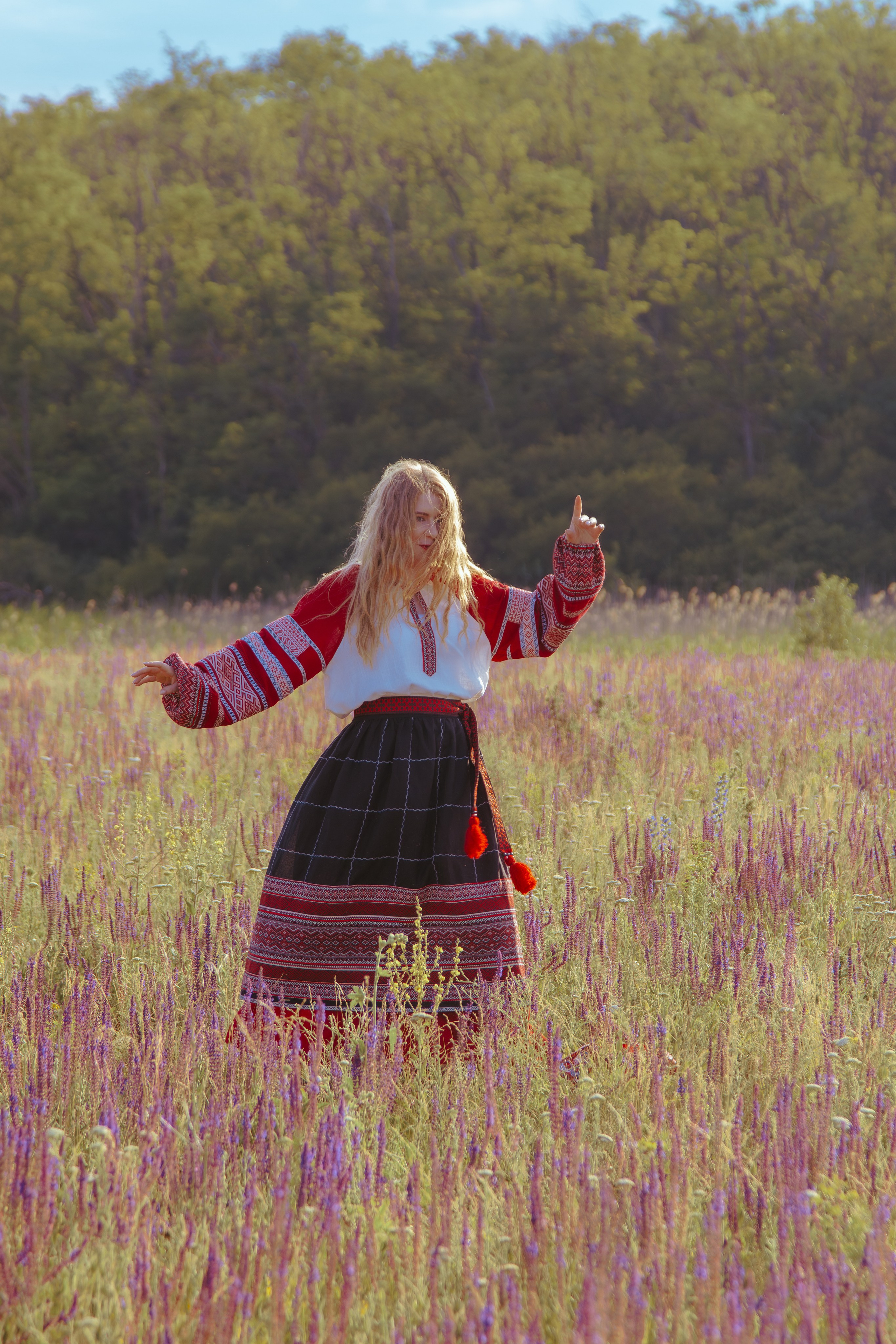 Девушка в славянской одежде танцует в поле на фоне леса