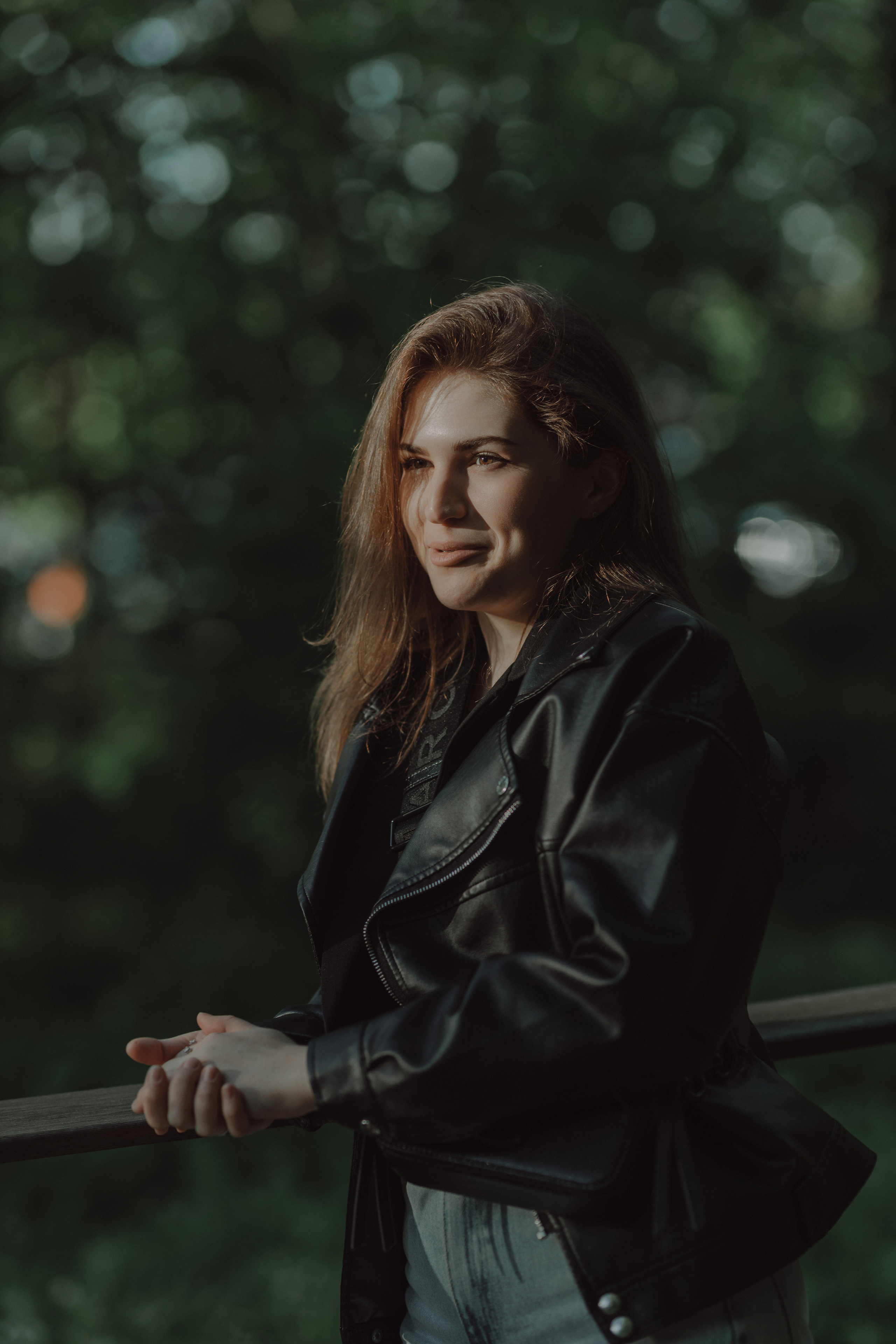уличная съёмка девушки в кожаной куртке на фоне зелени  
