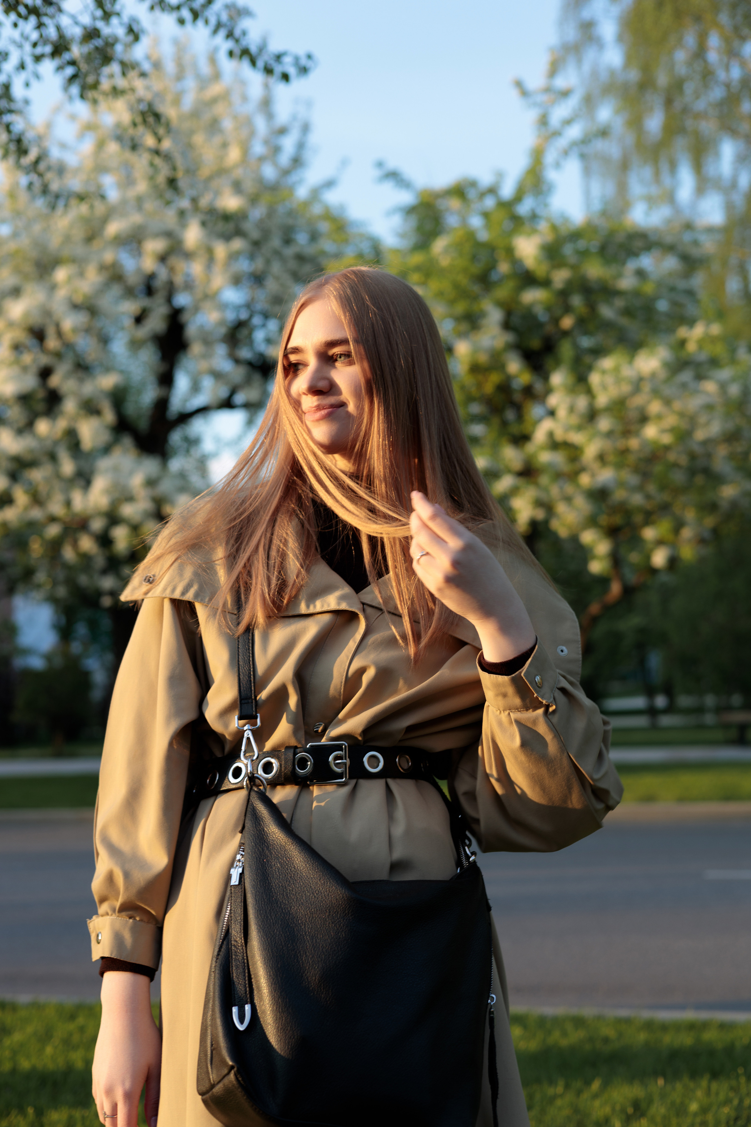 Портретная фотосессия молодой женщины в парке на фоне цветущих деревьев, съёмка в мягком свете