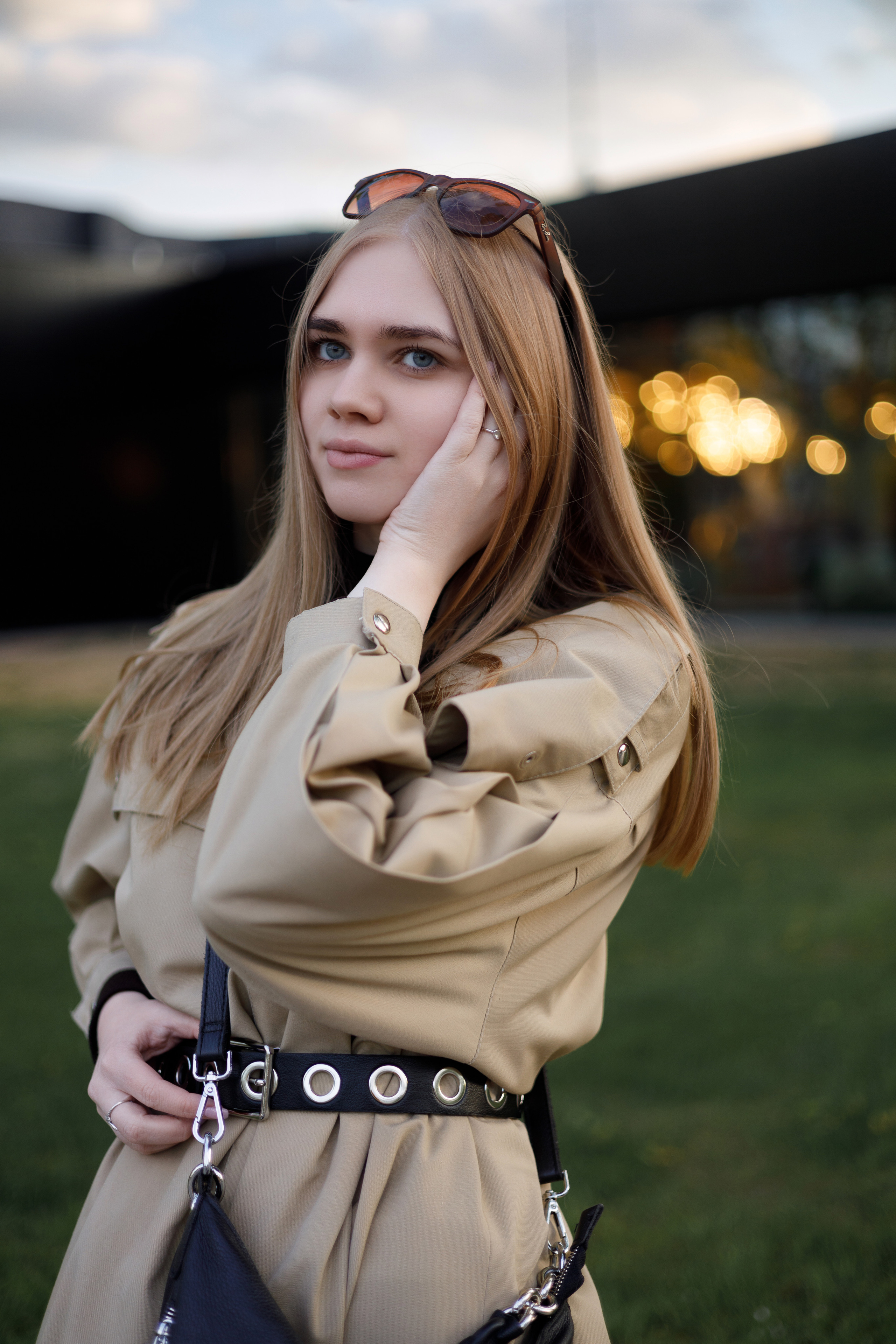 Портретная фотосессия девушки в бежевом плаще, профессиональная съёмка на фоне огней города на закате