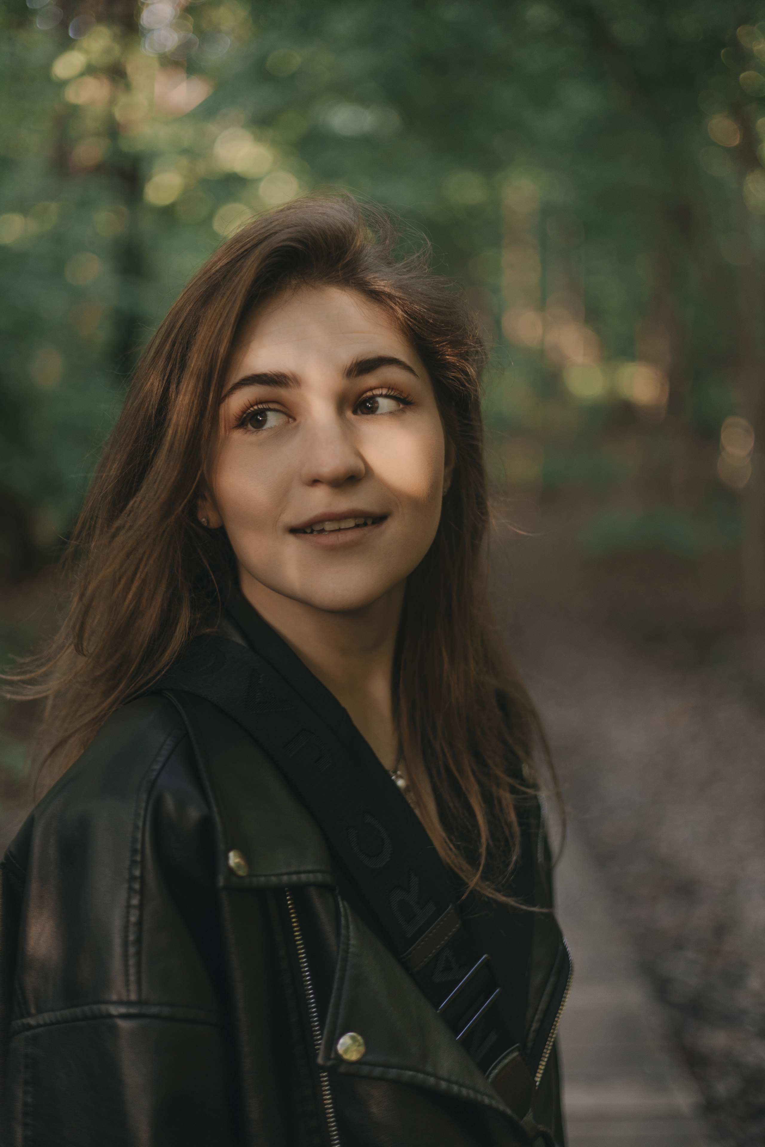 уличная съёмка девушки в кожанке на фоне деревьев, фотосессия в парке