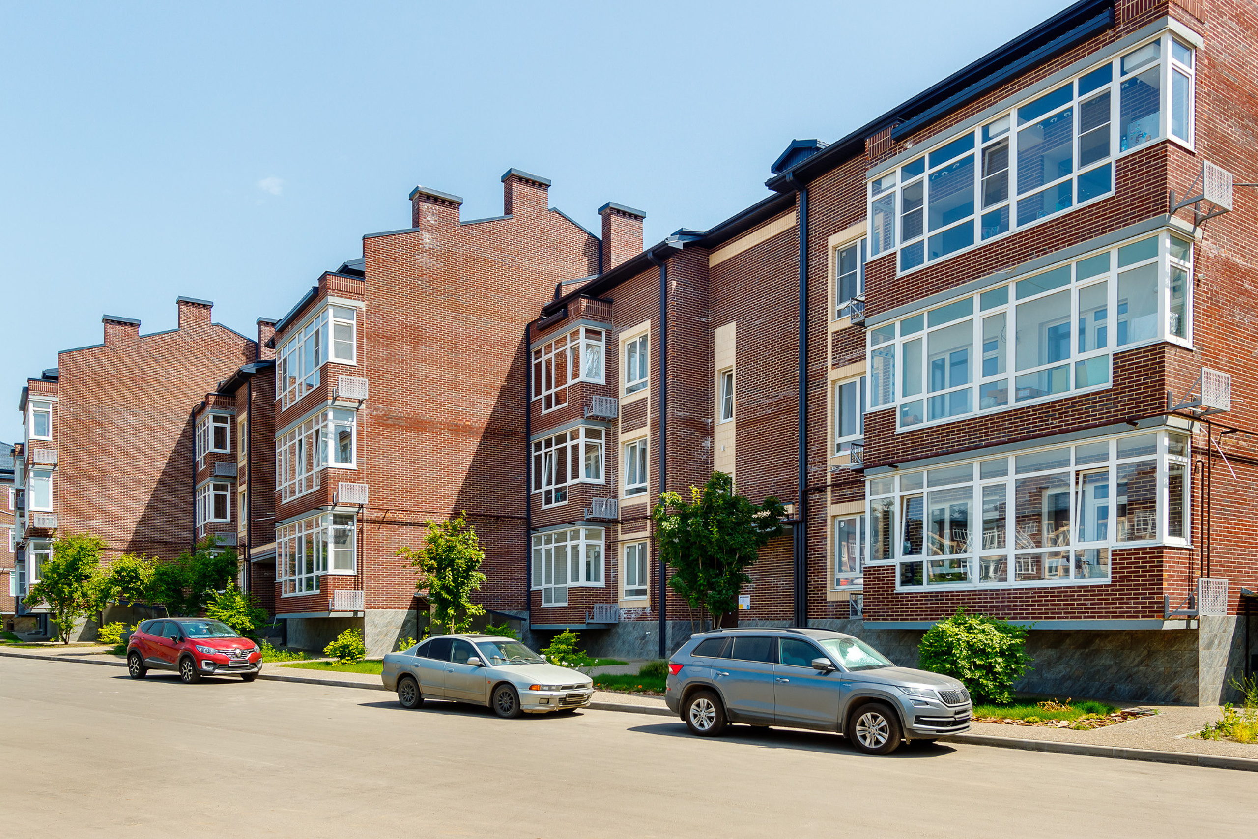 Фасад трёхэтажного жилого комплекса с припаркованными перед ним автомобилями