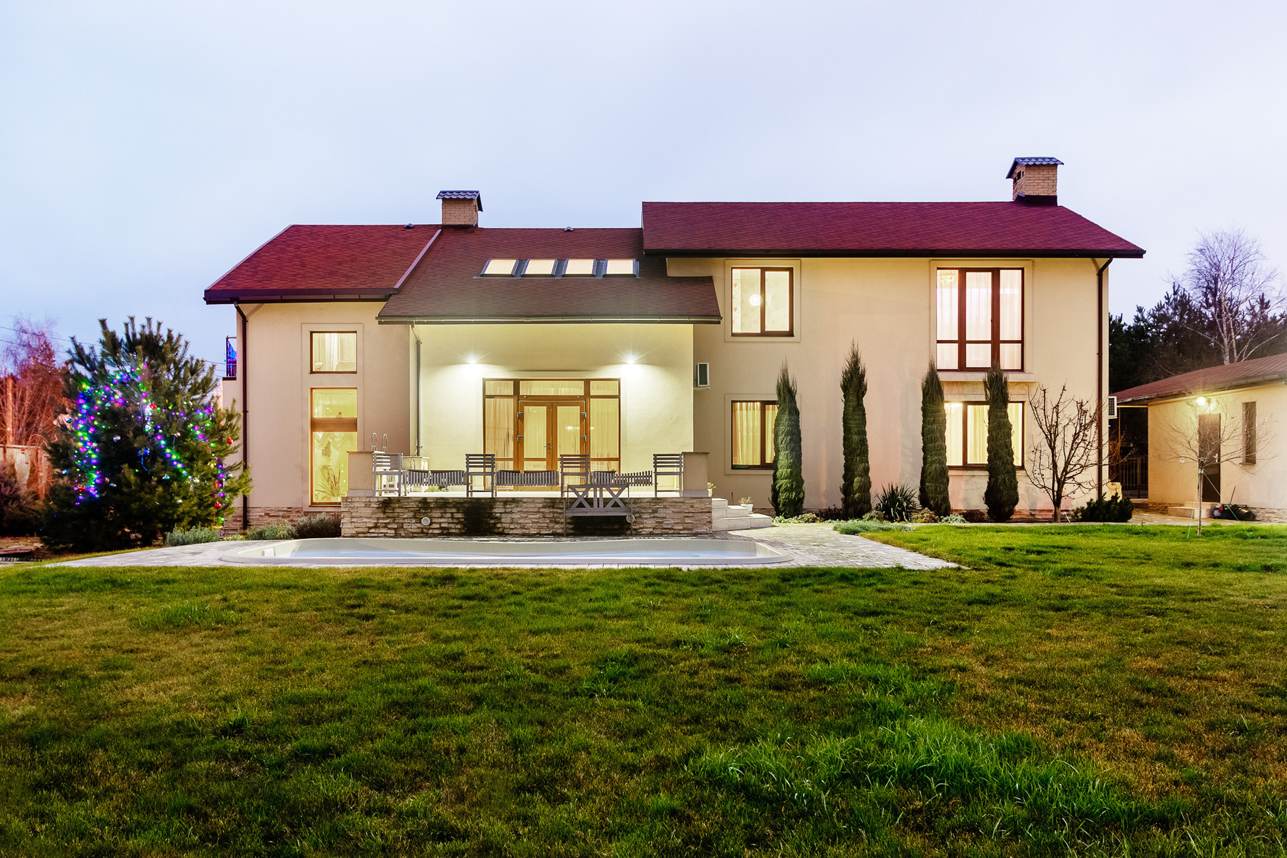 Фасад двухэтажного загородного дома с лужайкой и бассейном в вечернее время