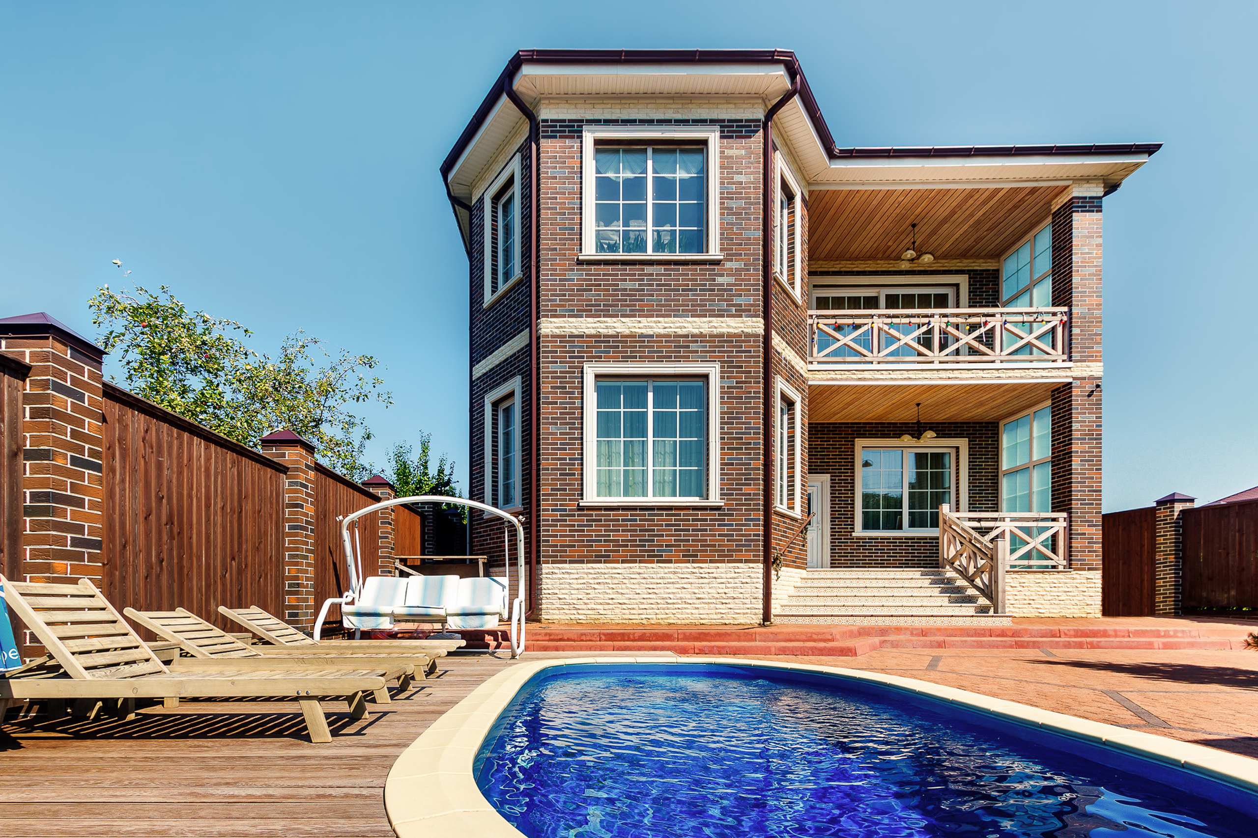 Двухэтажный кирпичный загородный дом с бассейном и зоной отдыха перед ним