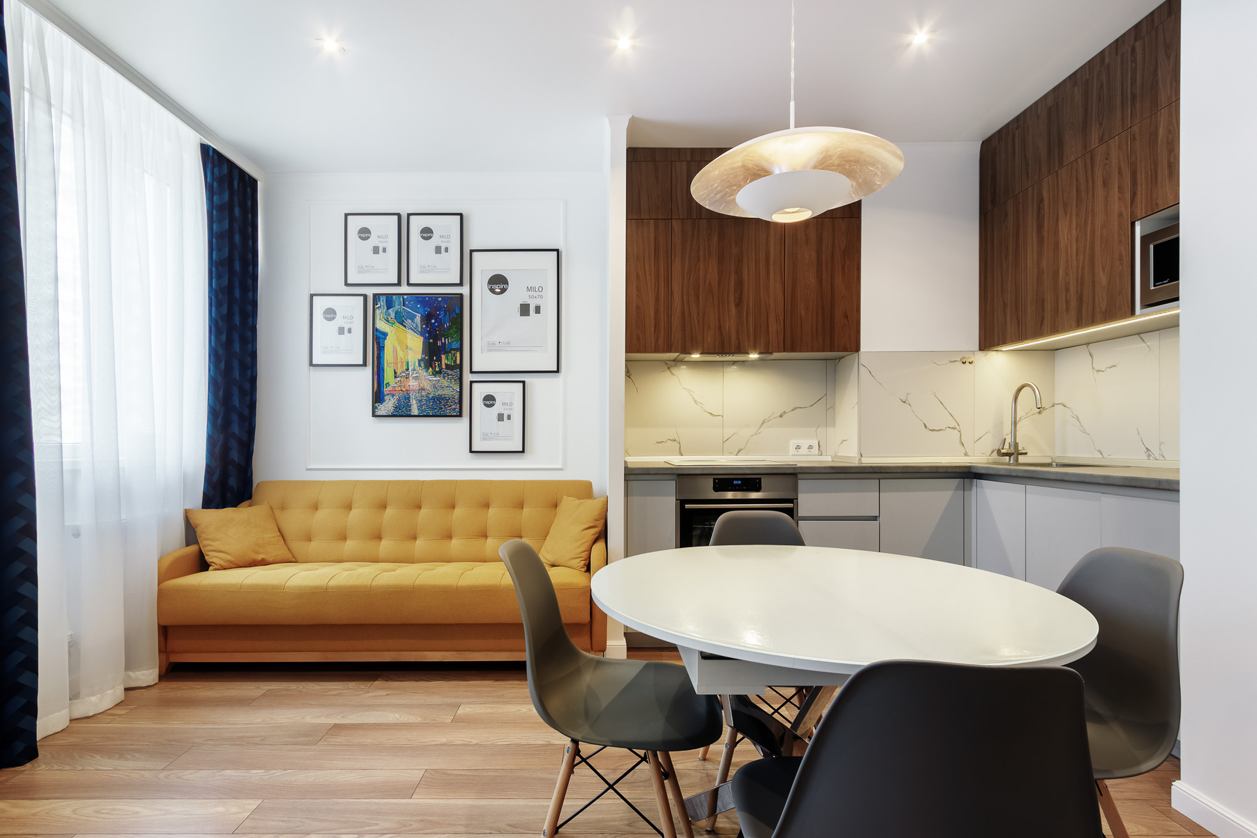 Квартира-студия с угловой кухней, круглым обеденным столом и жёлтым диваном