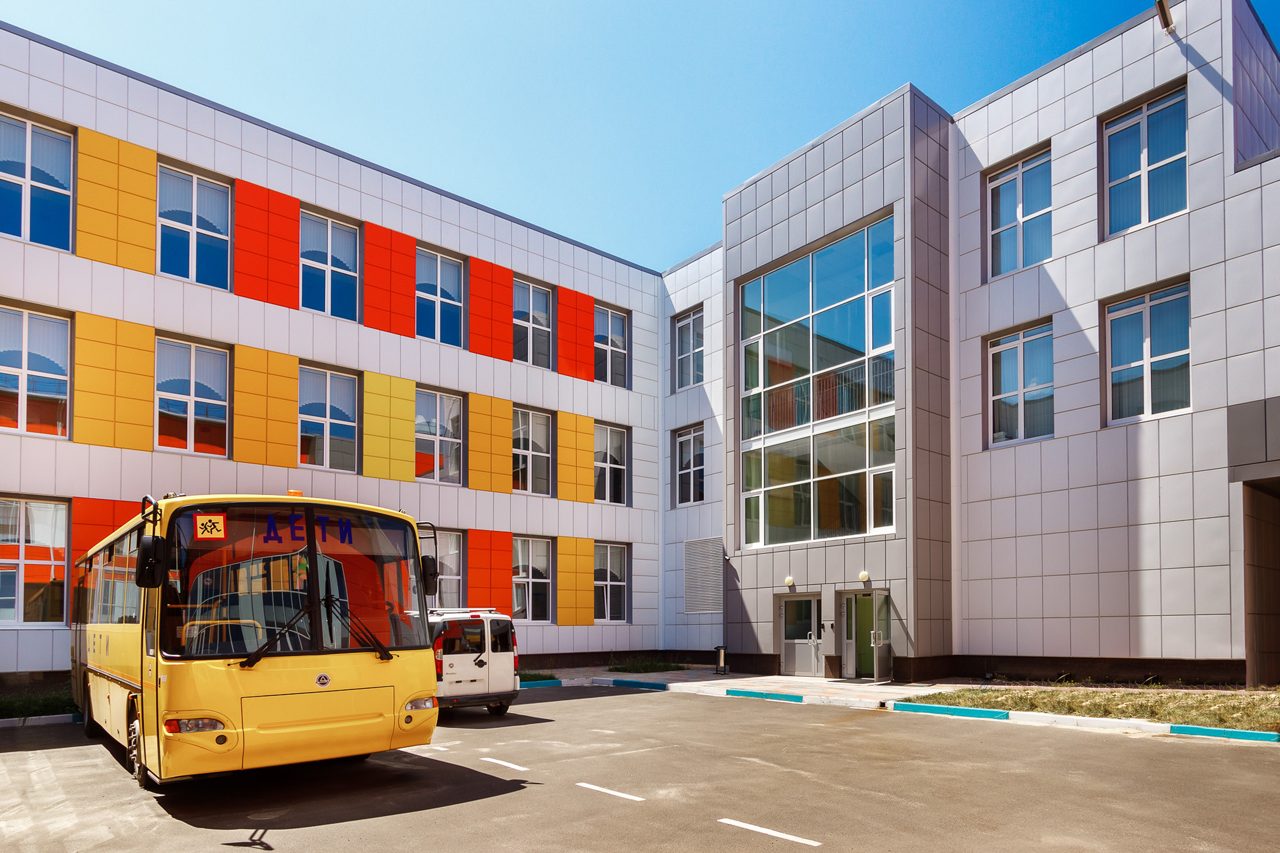 Внутренний двор школы с жёлтым автобусом для перевозки детей на парковке