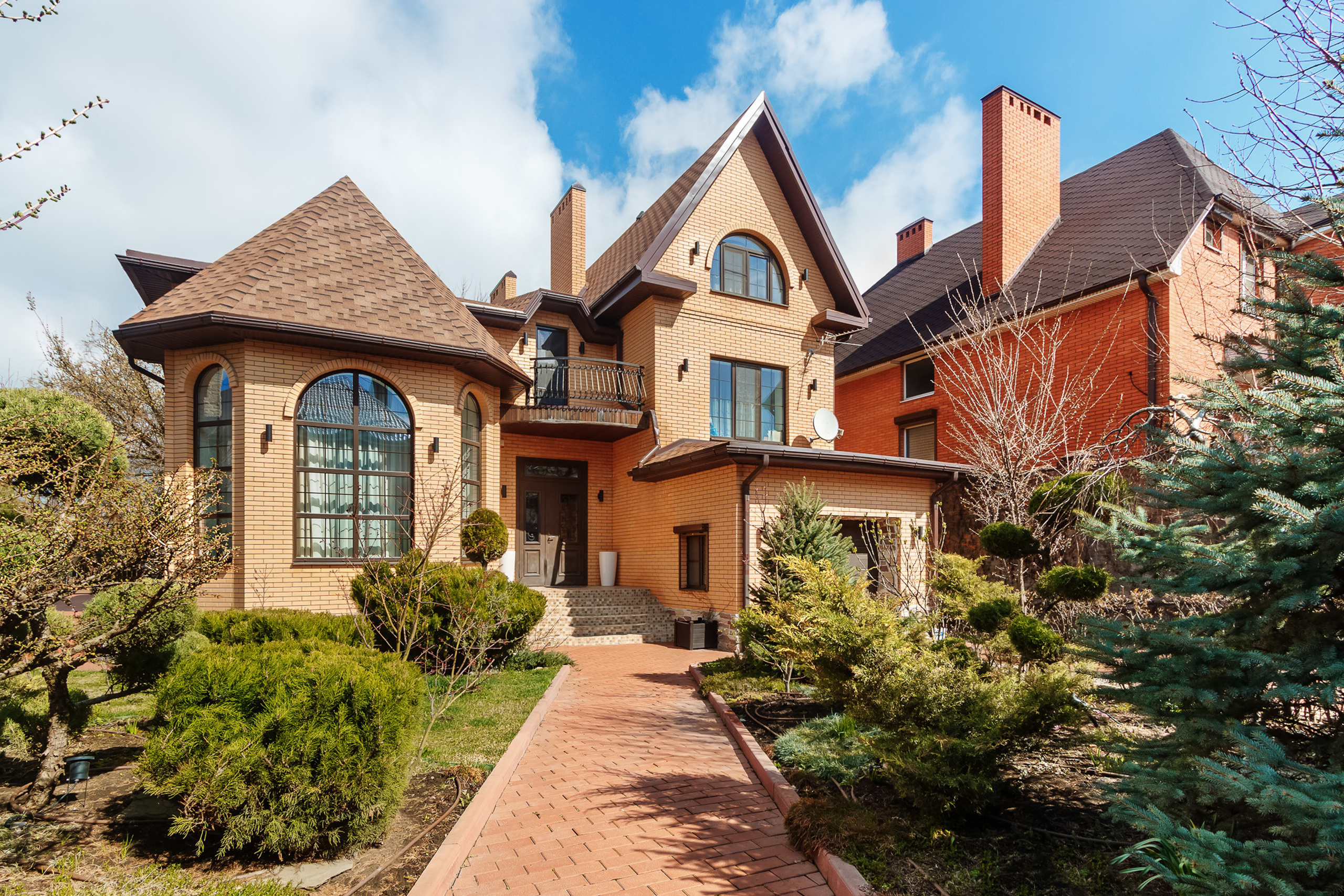 Фасад частного загородного дома с дорожкой и хвойными деревьями перед ним