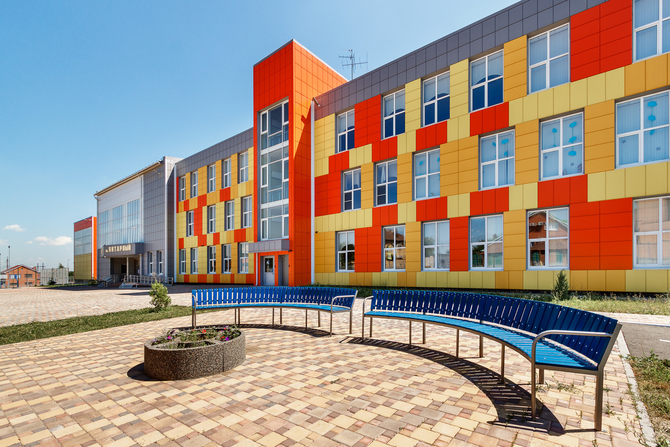Фасад большой современной школы с лавочками перед зданием