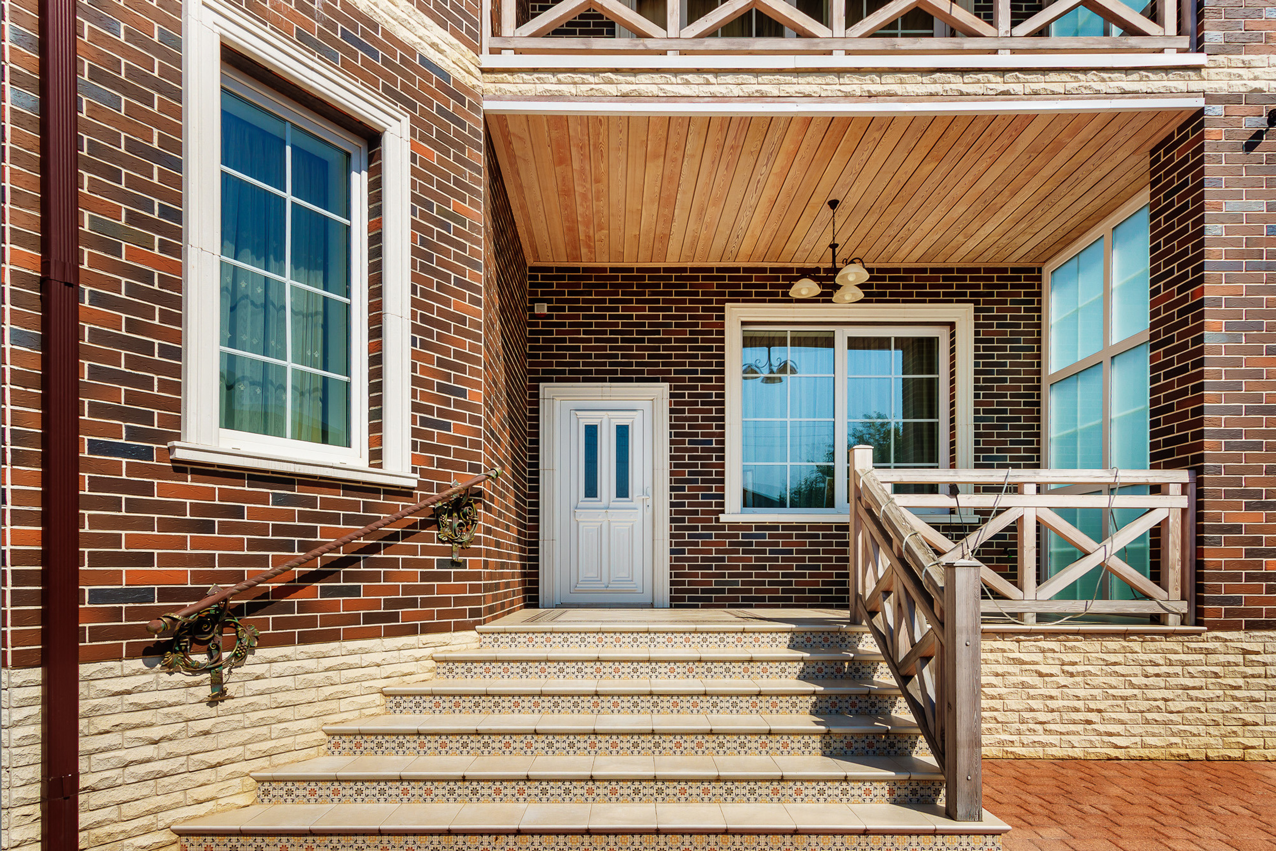 Входная группа кирпичного загородного дома с лестницей и верандой