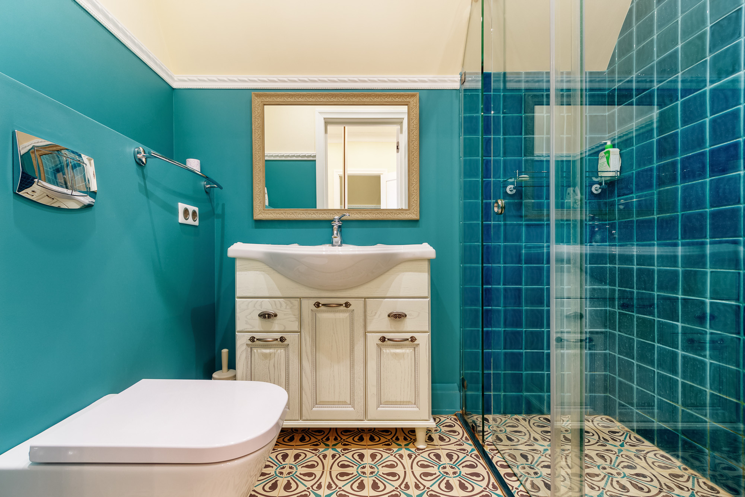 Интерьер ванной комнаты в цианового цвета с душевой кабинкой, белым умывальником и унитазом