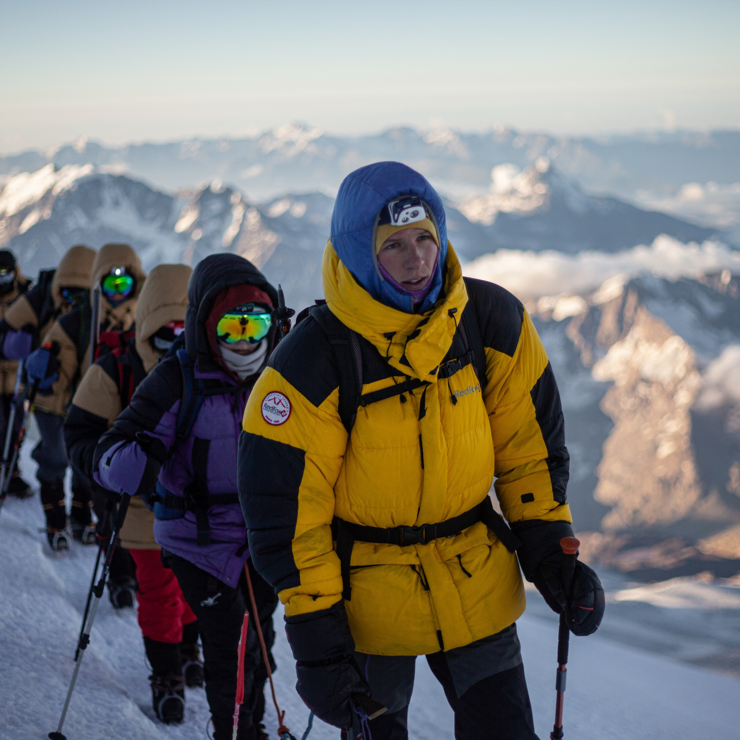 * Группа альпинистов на южном склоне Эльбруса.* Яркие куртки и каски.* Вид на горные вершины.* Альпинист закрепляет верёвку.