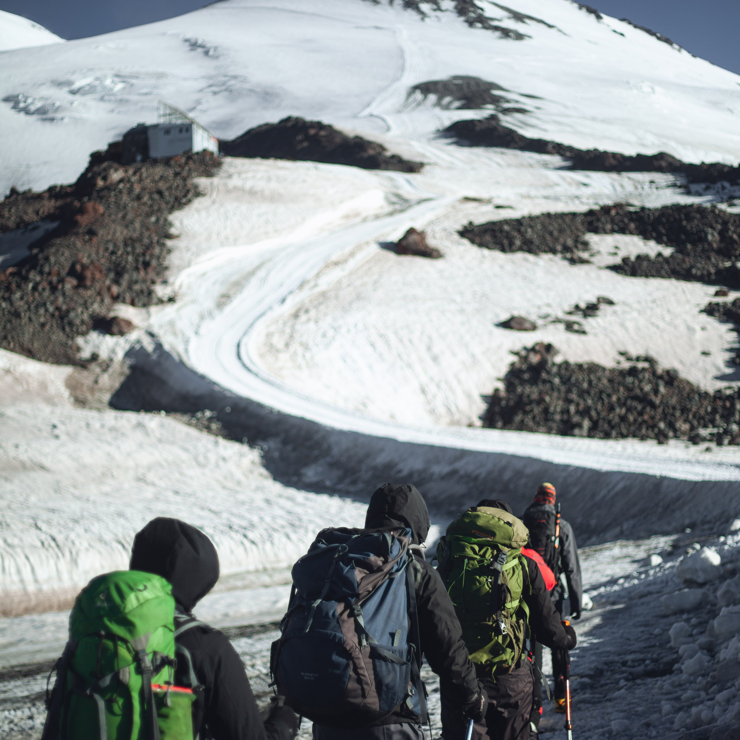 * Альпинисты в ярких куртках и касках.* Восхождение по южному склону Эльбруса.* Заснеженные горные вершины на фоне.* Закрепление страховочной верёвки.