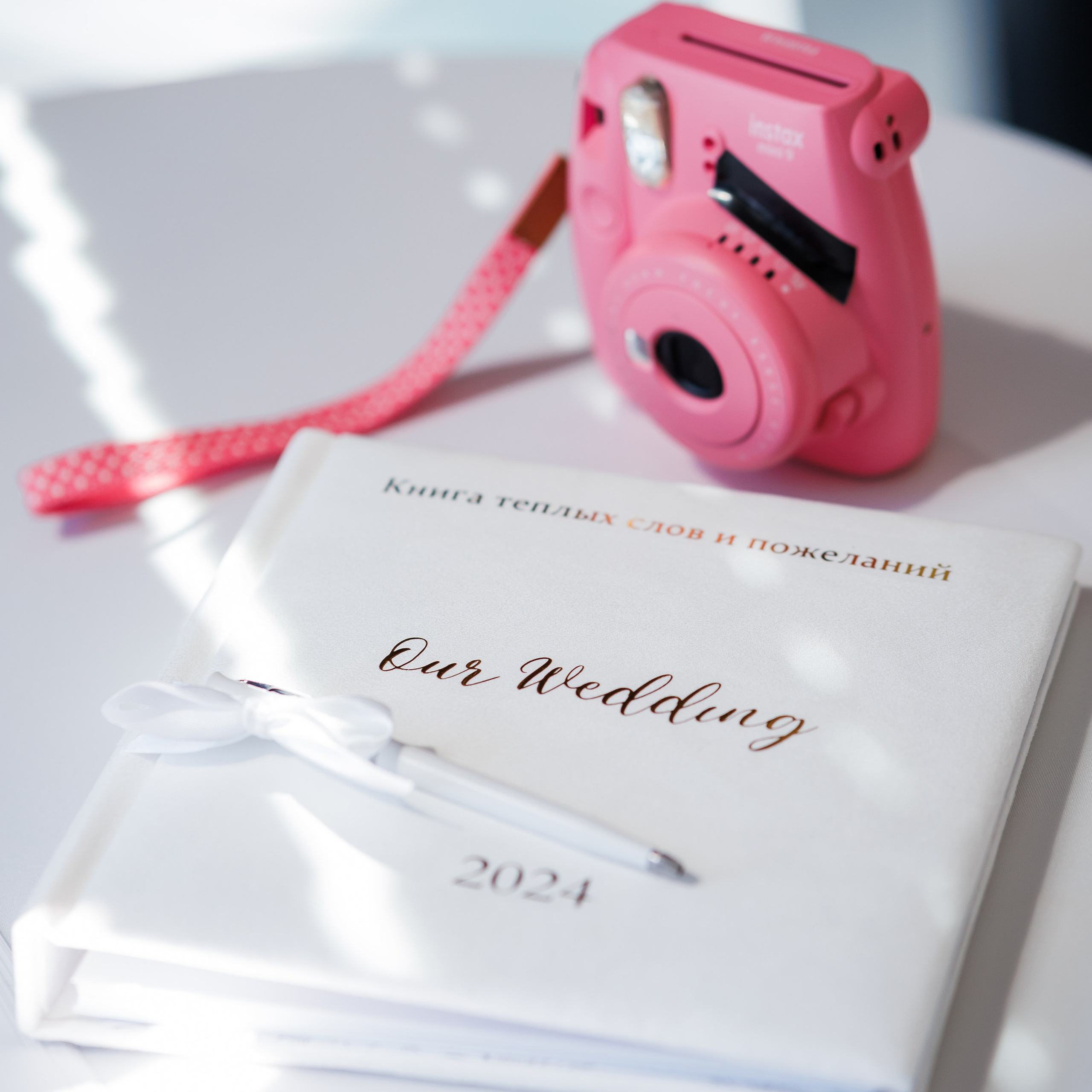 Фотоаппарат моментальной печати Кодак и альбом пожеланий для молодожёнов на свадебном торжестве. На фото изображены элементы праздничной атмосферы, где гости могут оставлять свои поздравления и снимки для создания памятных воспоминаний для пары.