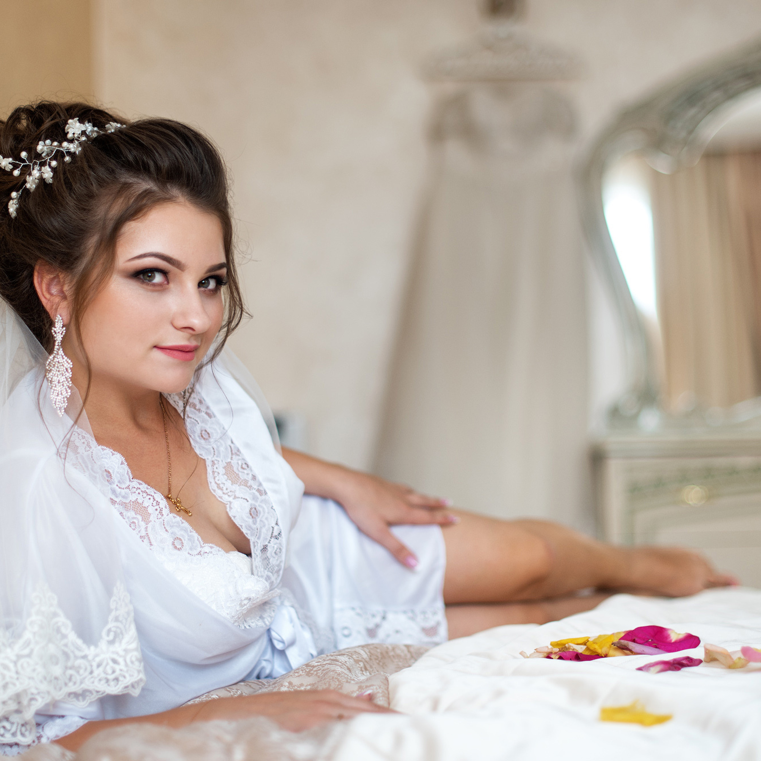 Невеста лежит в легком шелковом халате на кровати с лепестками роз в гостиничном номере Аквамарин 