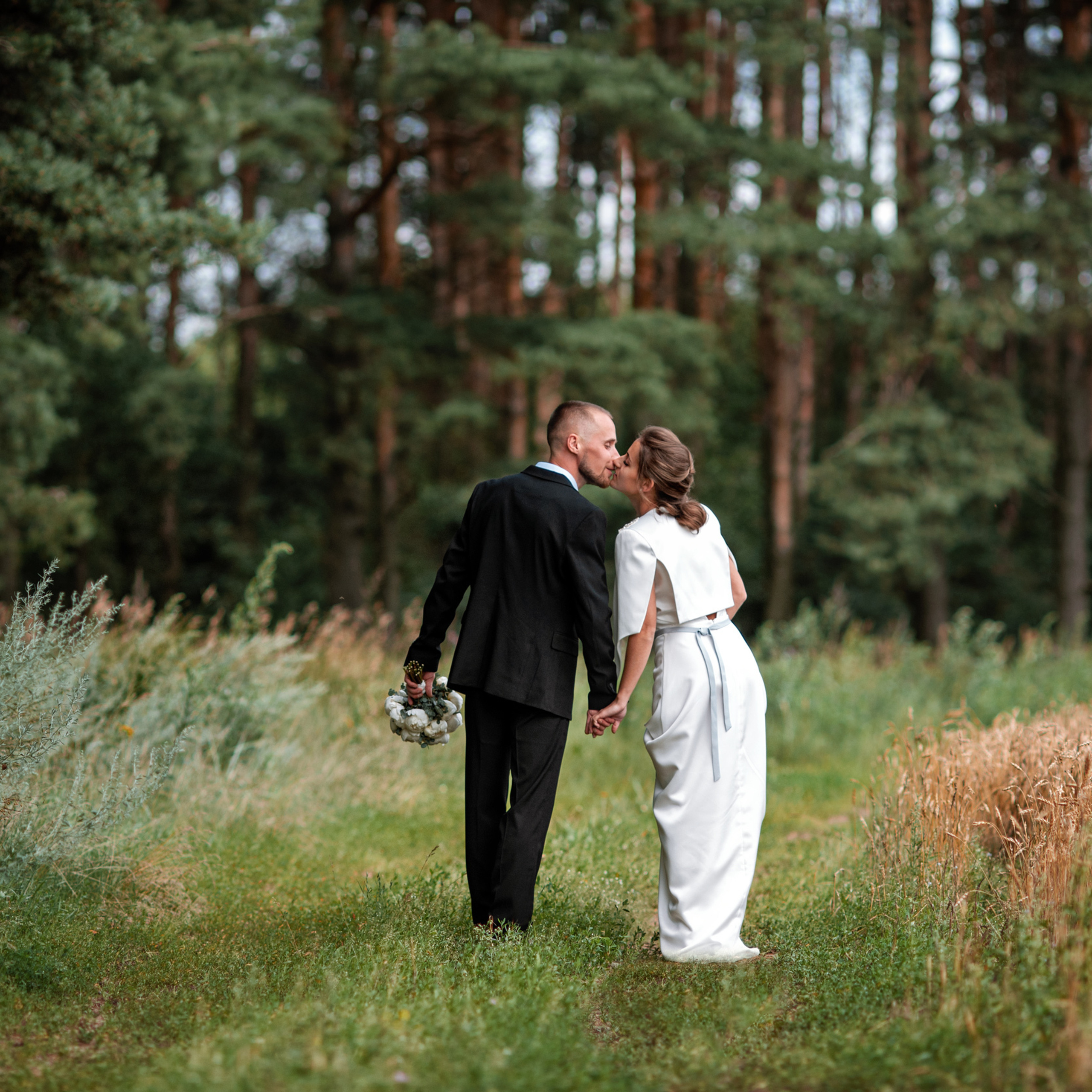 Молодожены идут за руки по проселочной дороге на опушке соснового бора в Подмосковье недалеко от города Клин