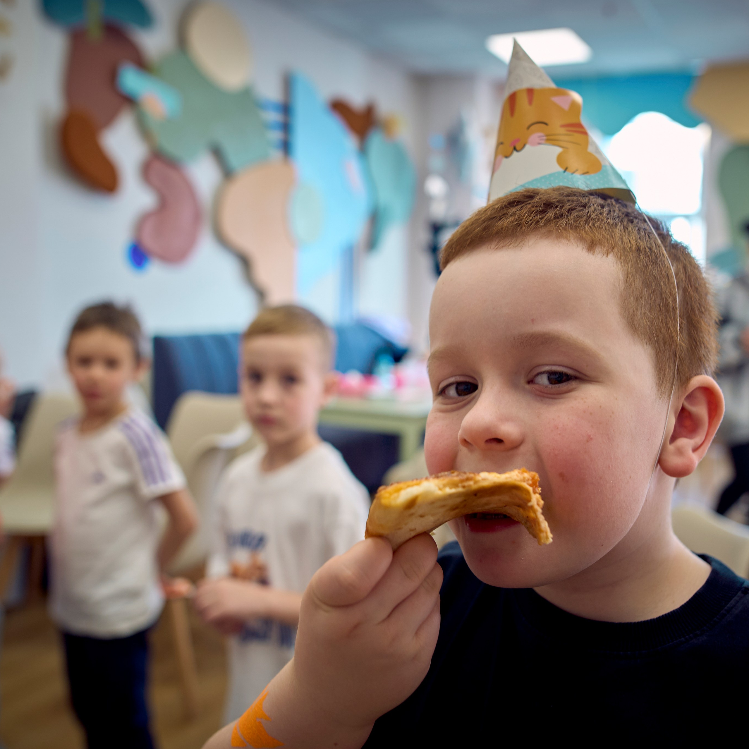 Мальчик на фоне своих друзей ест пиццу