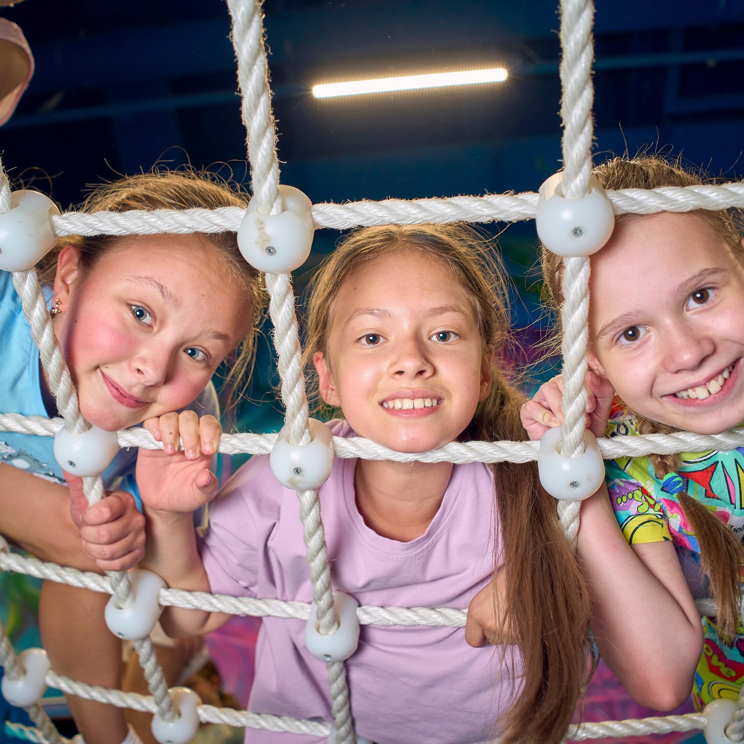 Девочки улыбаются через сетку из веревки