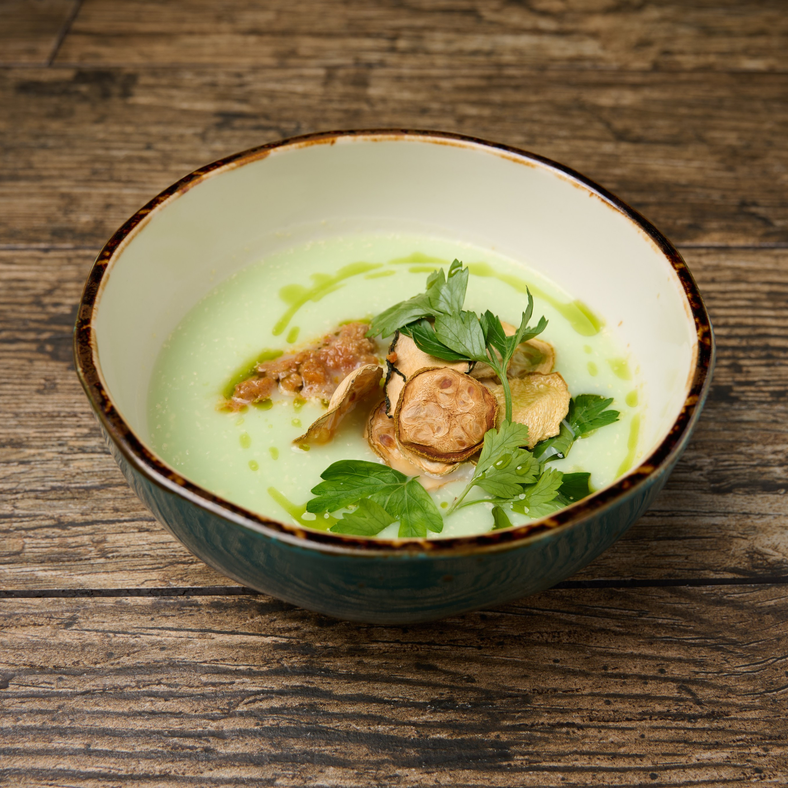 Кабачковый суп пюре, декорированный сушёным кабачком и свежей зеленью на деревянном столе