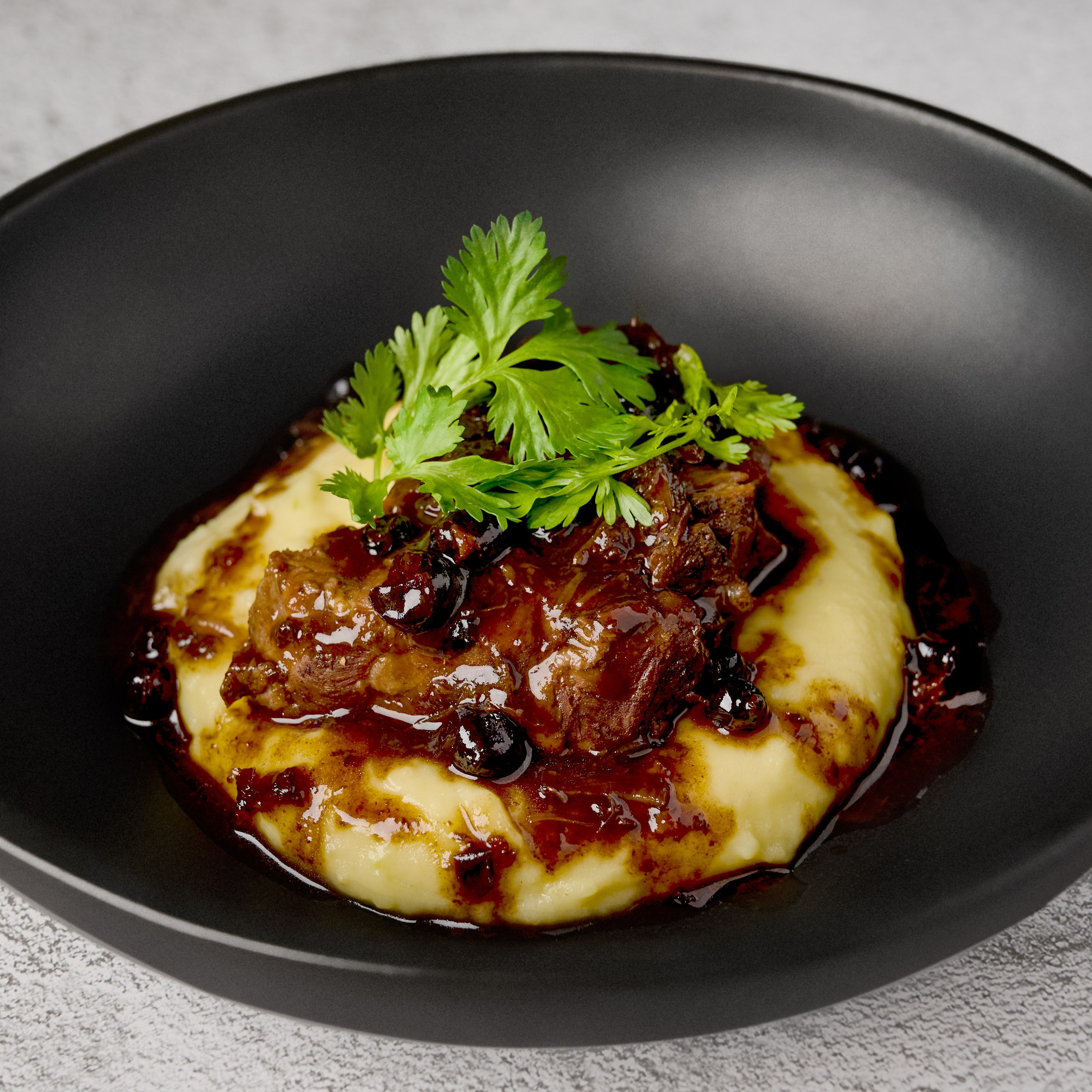 Картофельное пюре с мясом и ягодным соусом на черной тарелке и сером фоне