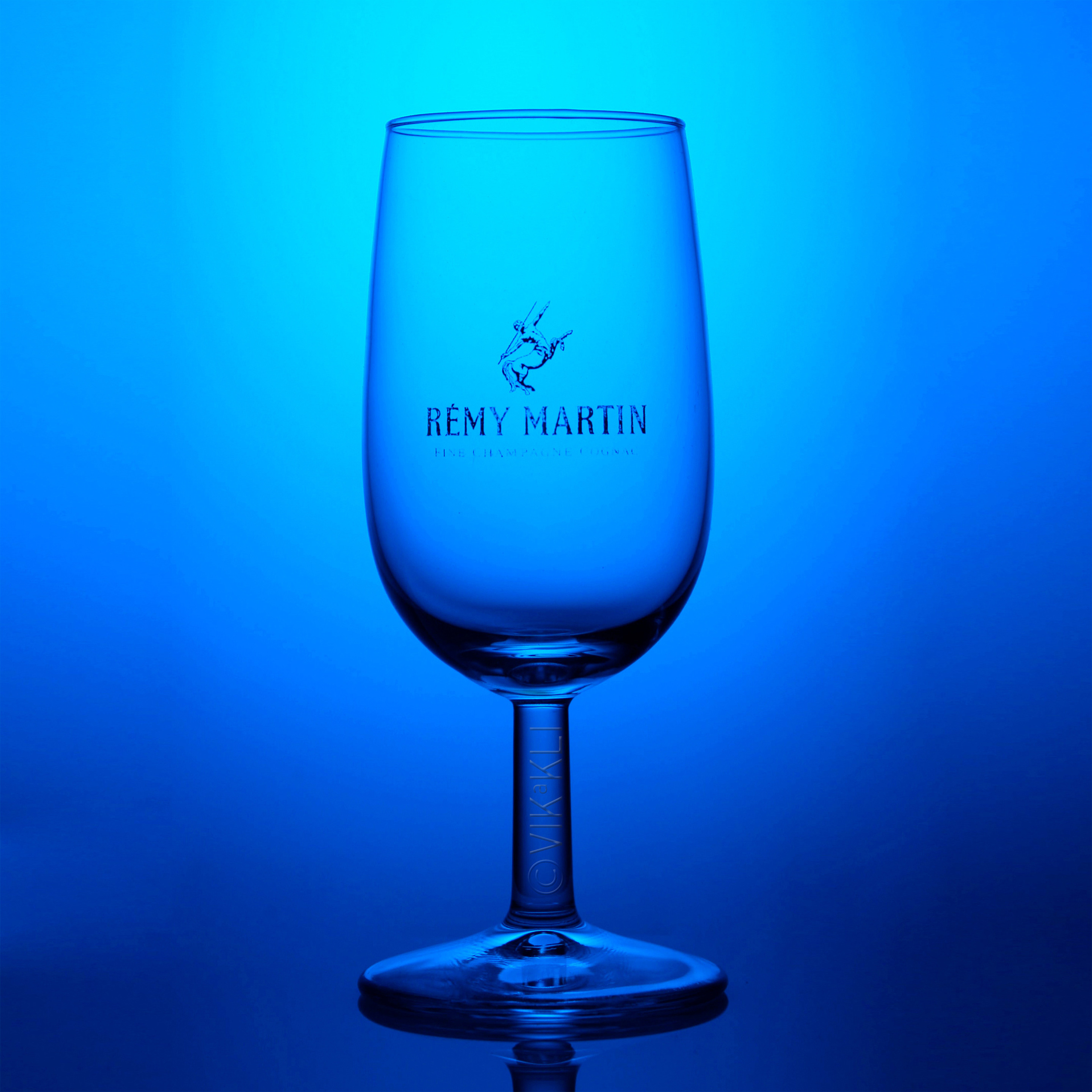 Стеклянный бокал Remy Martin на синем фоне.. Предметное фото.