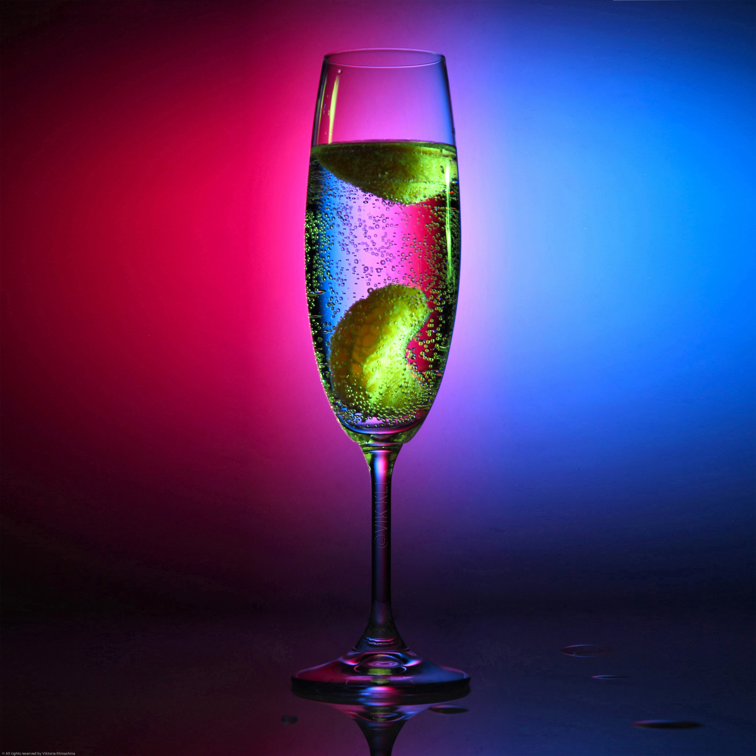 Стеклянный бокал с шампанским на розово-голубом фоне. Предметное фото..