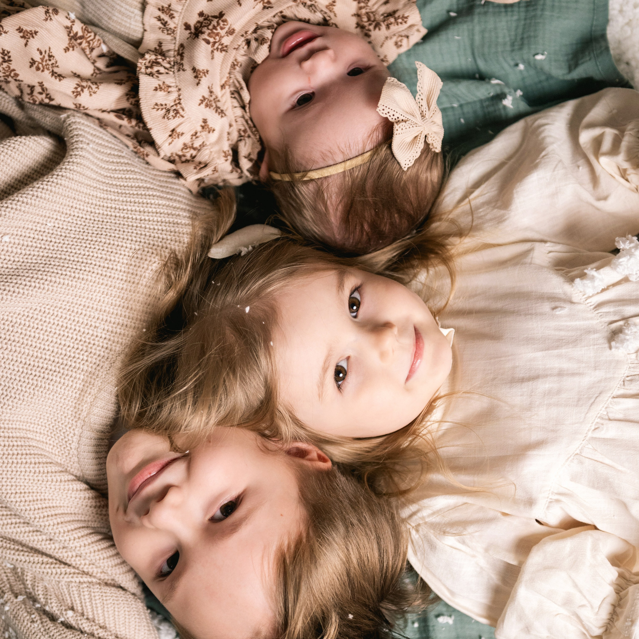 Детская и семейная новогодняя фотосессия в Новосибирске — три девочки лежат на полу в хлопьях снега, нежный праздничный кадр