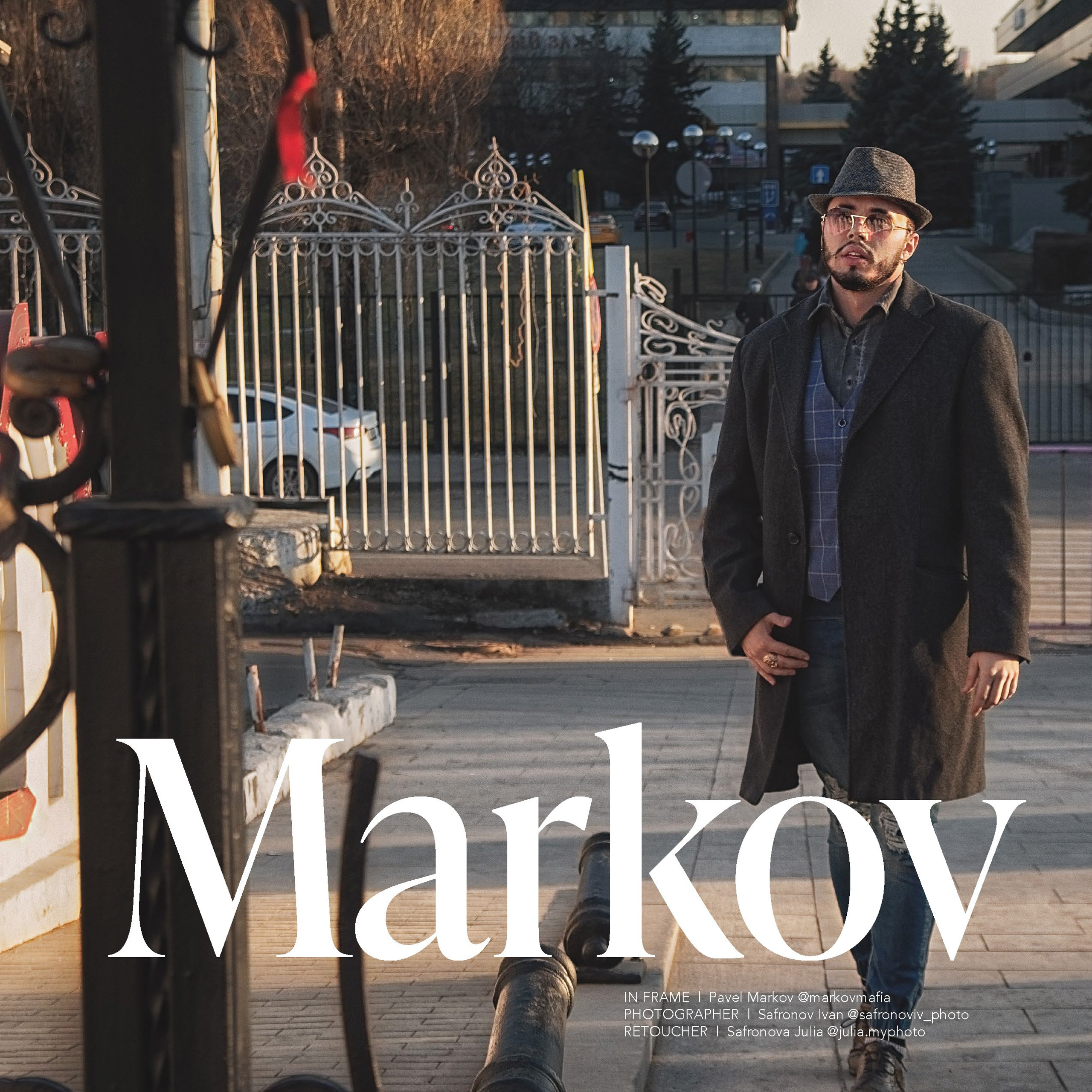 мужчина в стильном классическом образе: тёмное пальто, жилет в клетку, рубашка, джинсы, шляпа и очки. Он стоит на улице в расслабленной позе, слегка наклонив голову, что придаёт портрету задумчивость и характер. На переднем плане — декоративная металлическая ограда с изящными завитками, которая частично обрамляет кадр. За спиной модели видны кованые ворота, старинная пушка, городские здания и деревья без листвы, что создаёт атмосферу урбанистического ретро. Тёплый свет заката подчёркивает текстуры одежды и металлических элементов, добавляя глубину и драматизм снимку.Заголовок«Городской джентльмен: гармония стиля и урбанистики»Ключевые словапортретный фотограф в Москве, фотограф Сафронов Иван, уличный стиль, классический образ, ретро-эстетика, городской пейзаж, закатное освещение, мужская мода, кованые элементы.