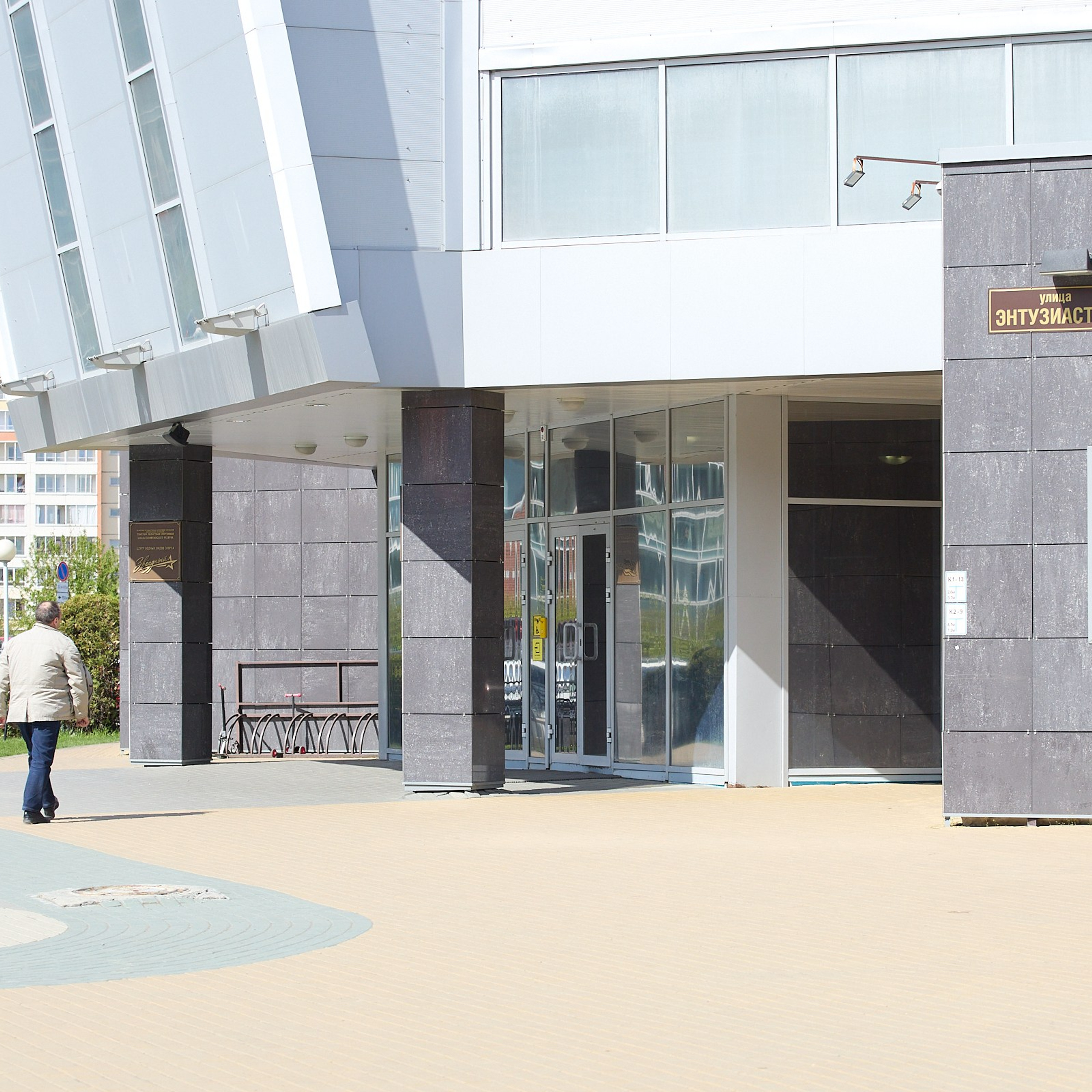 Фото входной группы и прилегающей территории бассейна «Звёздный» в Томске. Вид со стороны фасада. В кадре идущий человек со спины для масштаба.