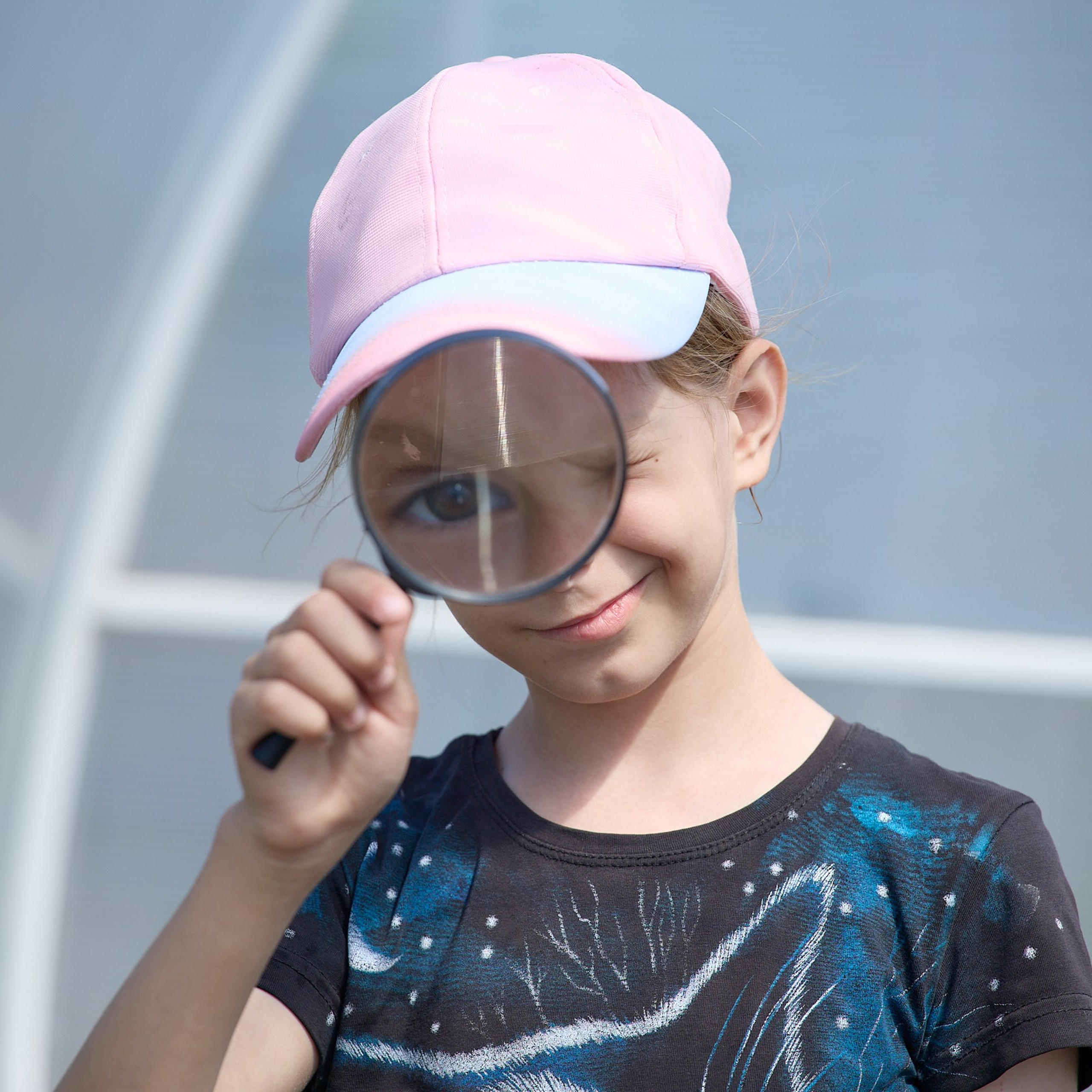 Девочка в розовой кепке смотрит через лупу
