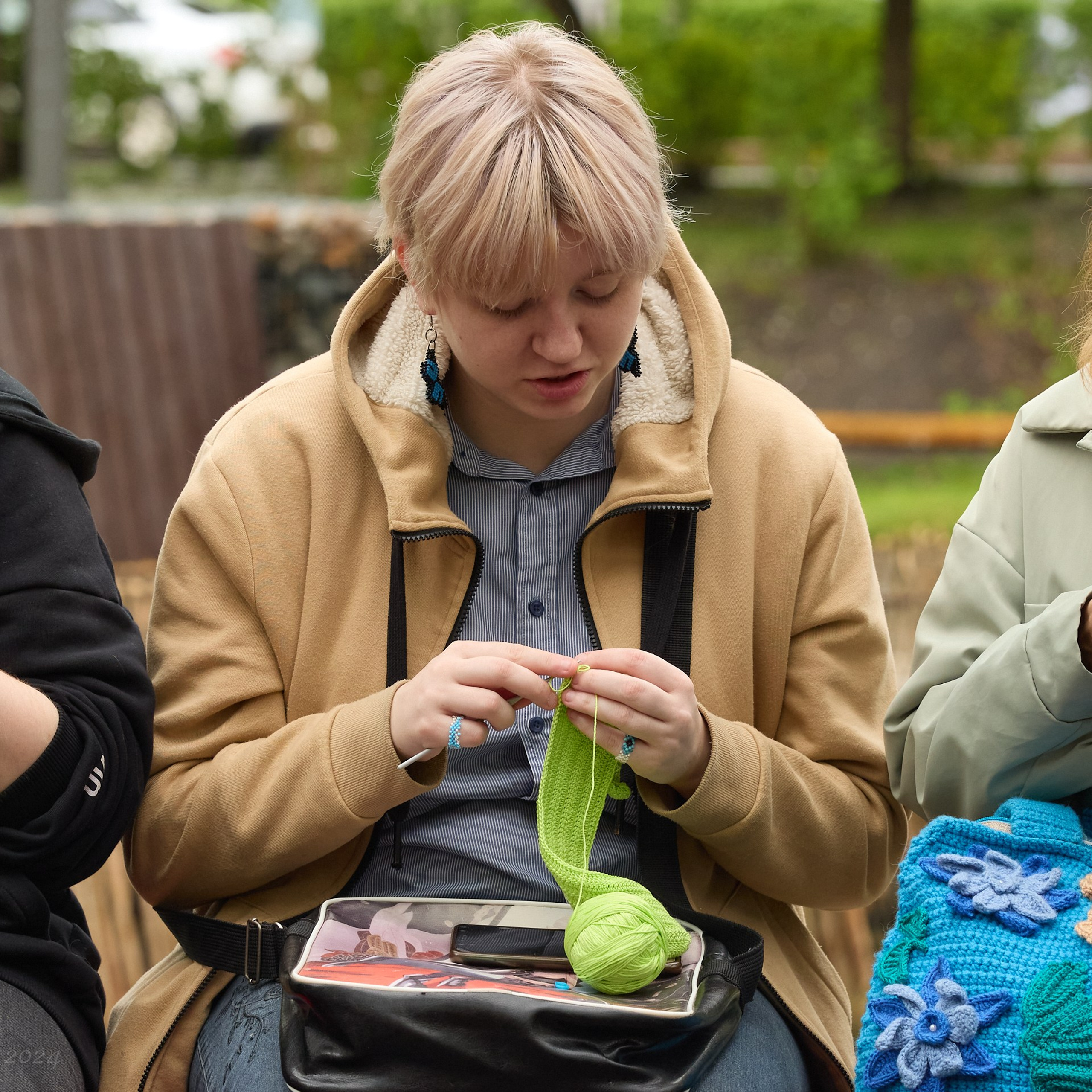 Блондинка с короткими волосами вяжет из зеленой пряжи.