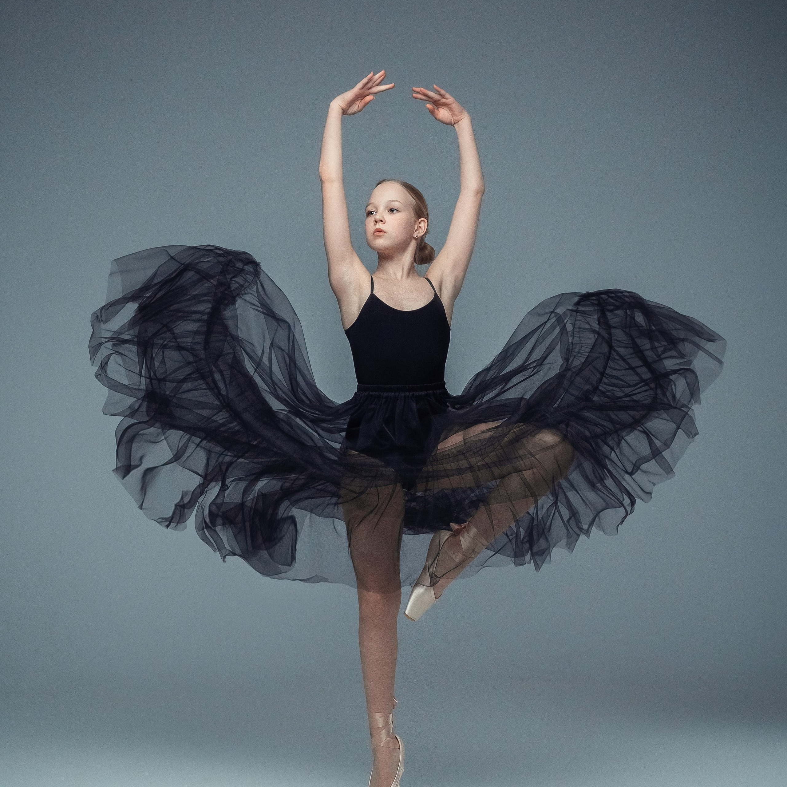 Гимнастка в элегантной позе выполняет элемент с лентой, плавно вытягивая ткань в динамичном движении, демонстрируя гибкость, грацию и выразительность художественной гимнастики